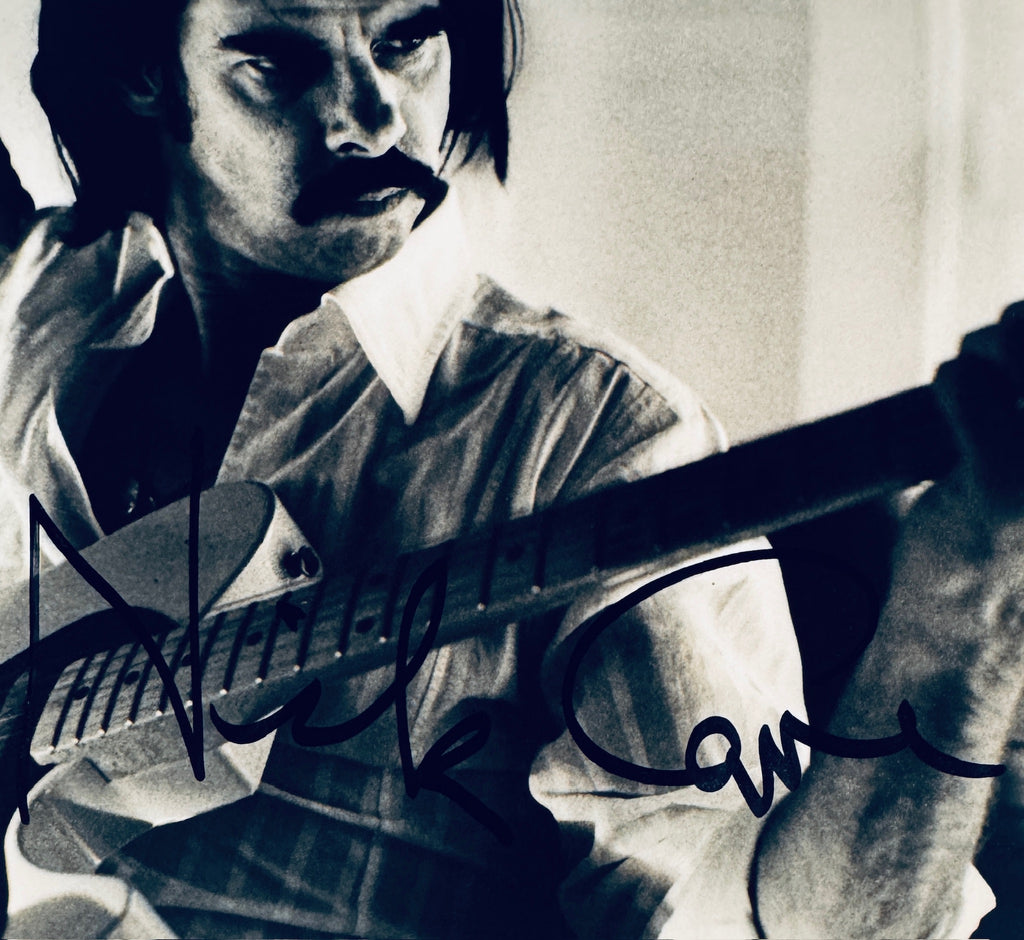 • Close-up detail of a genuine Nick Cave hand-signed autograph in black marker over a high-contrast black and white vintage music portrait photograph.
