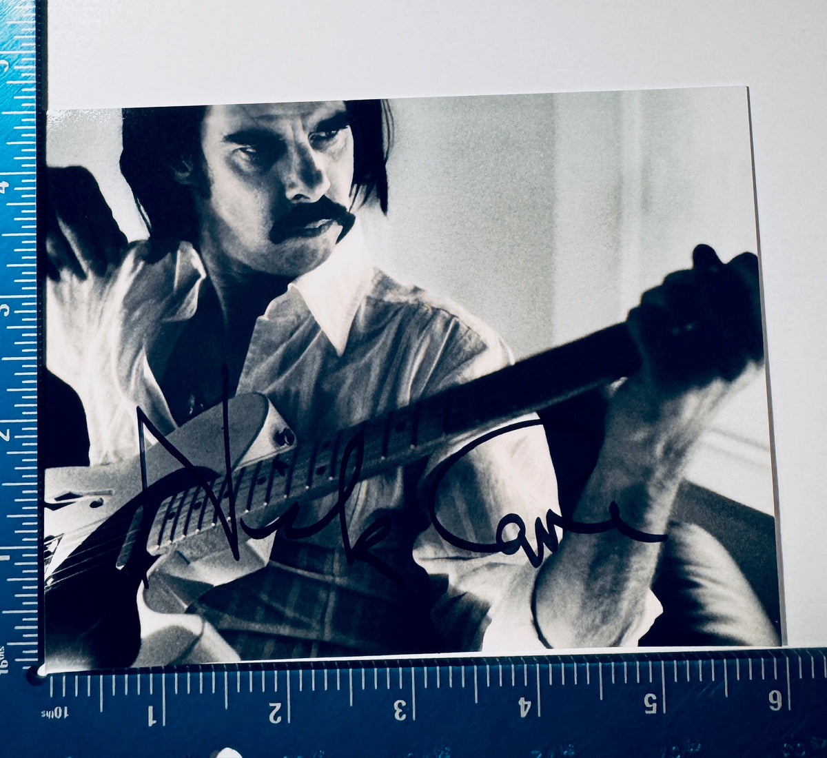 • Nick Cave autographed 4x6 black and white photograph featuring an authentic hand-signed signature, framed against a professional blue grading calibration ruler.
