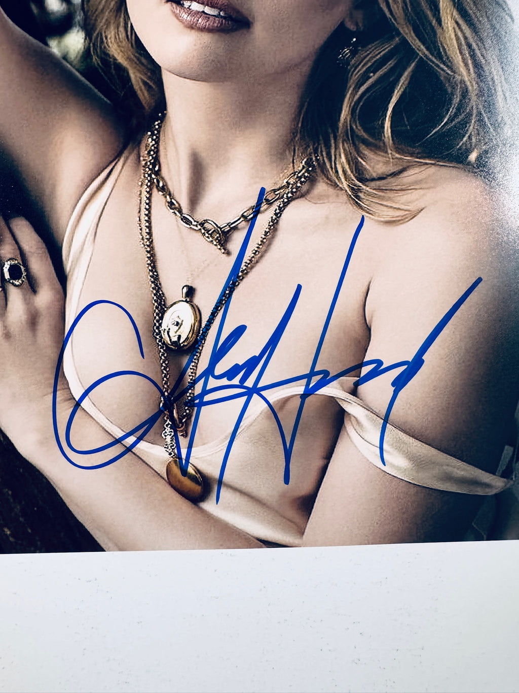 Close-up view of Amber Heard's blue signature across her chest and necklaces on the promotional photograph.