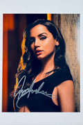 Signed full photo of Ana de Armas wearing a black top against a warm-lit wall, featuring a silver autograph.