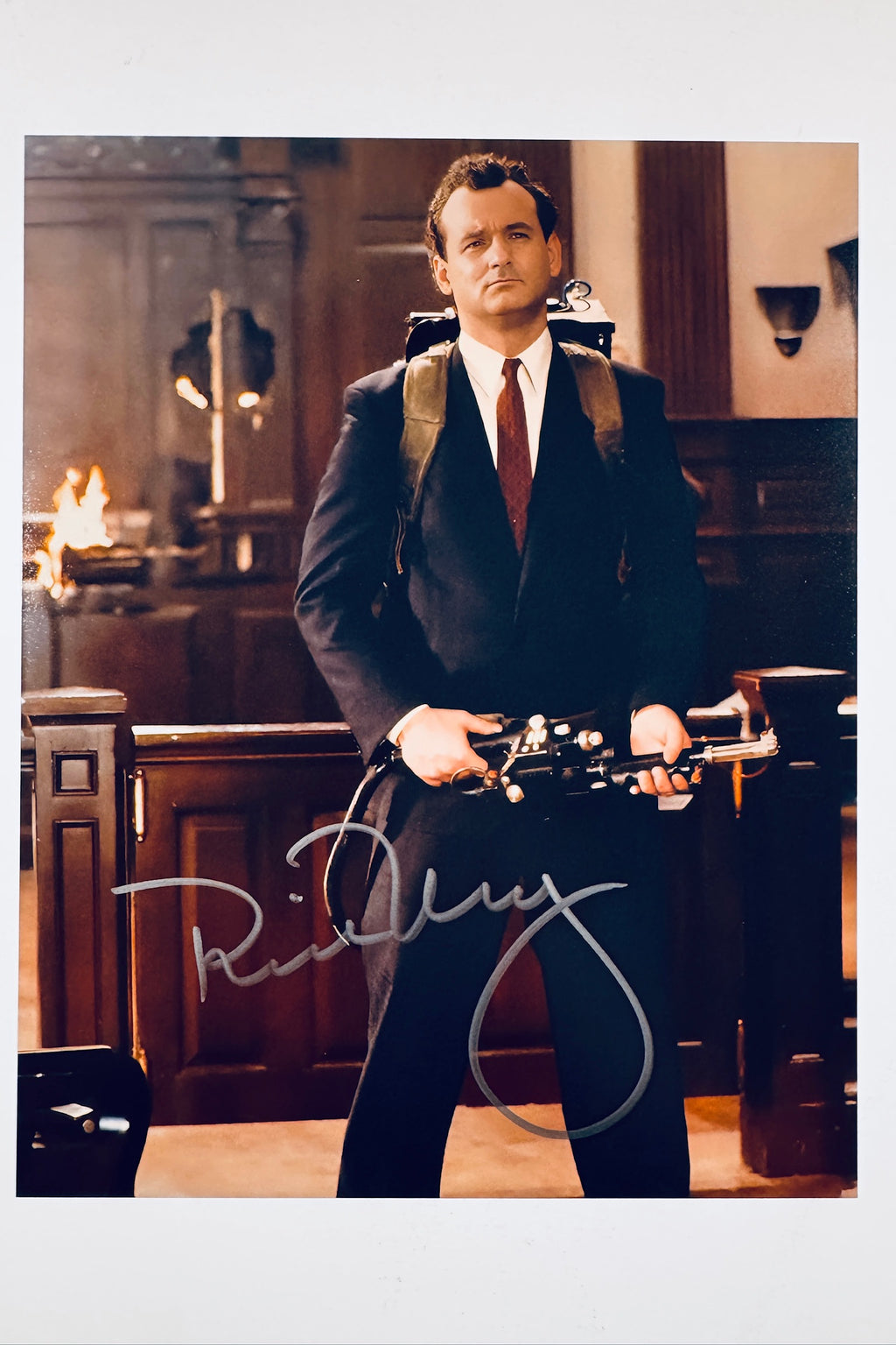 A portrait of Bill Murray as Peter Venkman wearing a dark suit and red tie, holding a proton pack wand, featuring a signature across the lower area.