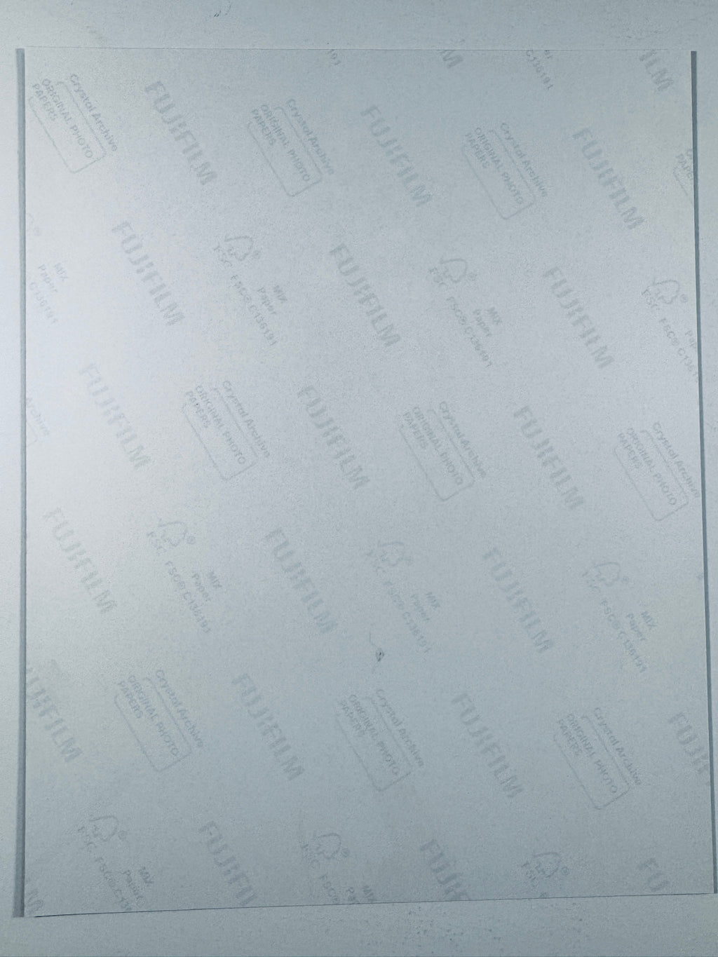 The plain white reverse side of a photographic print showing faint translucent watermark patterns and repeating Fujifilm paper logos.