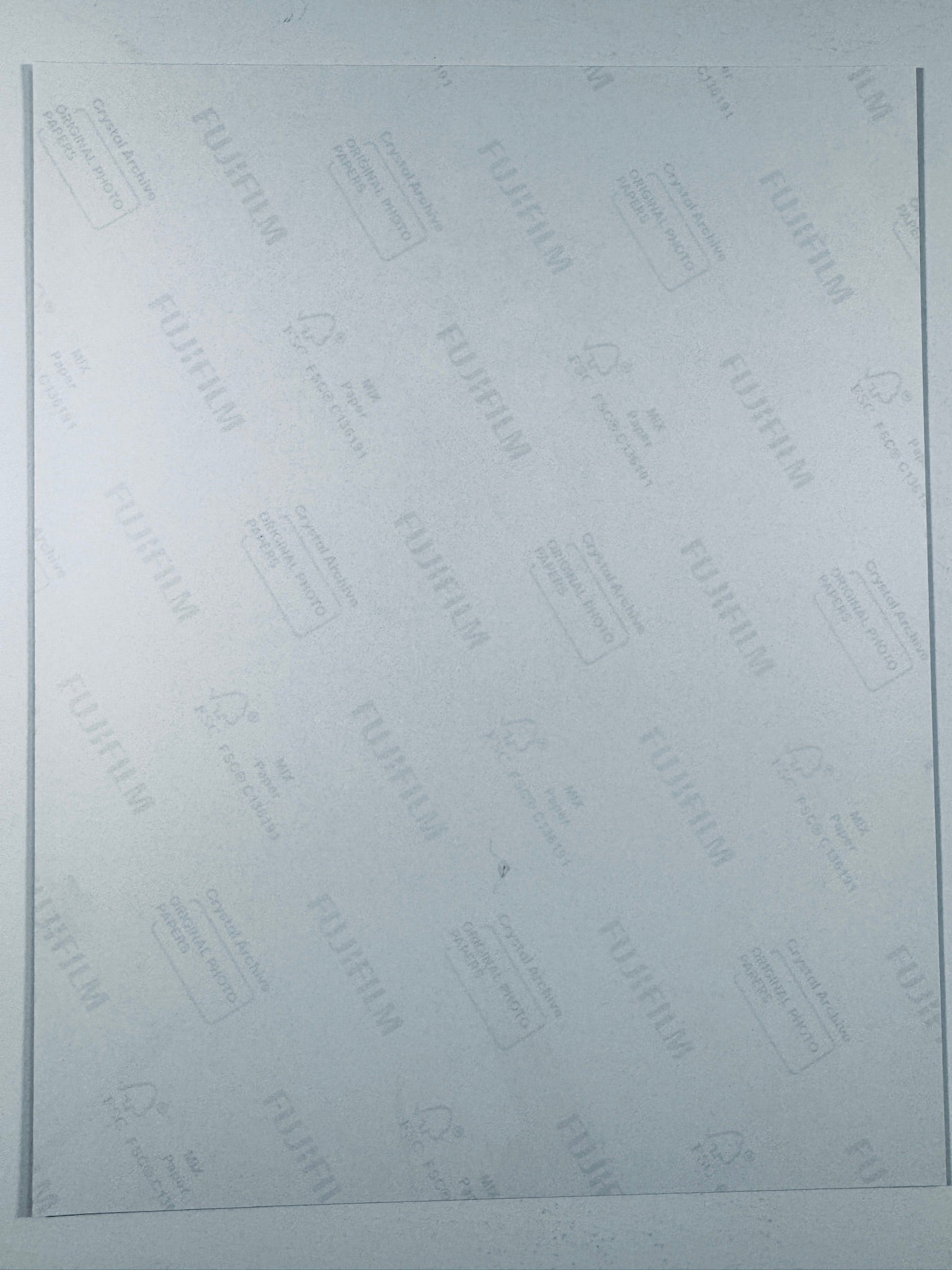 The plain white reverse side of a photographic print showing faint translucent watermark patterns and repeating Fujifilm paper logos.