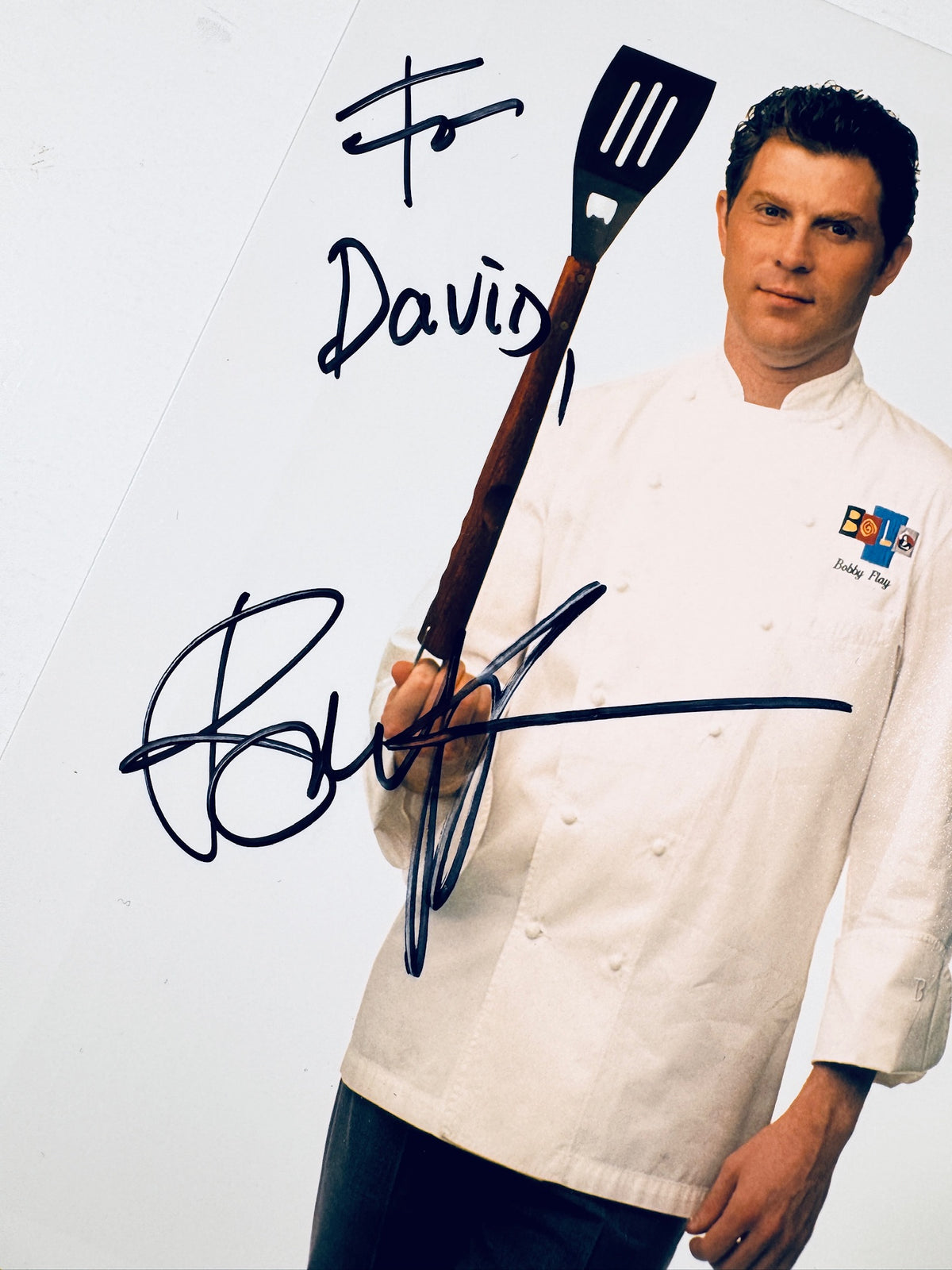 Close-up of Bobby Flay's black marker autograph and personalized inscription on a promotional photo.