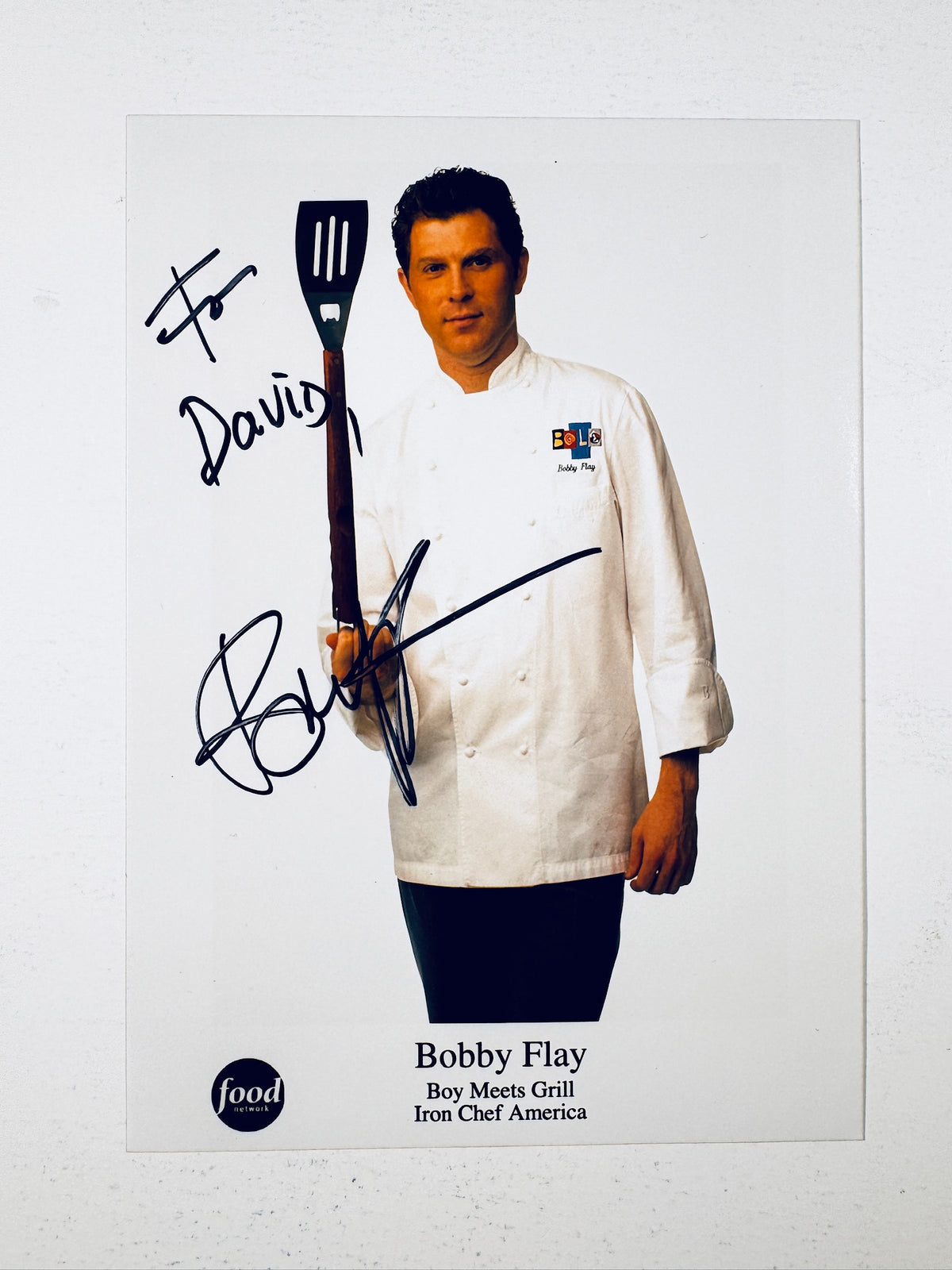 Autographed promotional portrait photo signed by chef Bobby Flay holding a spatula.