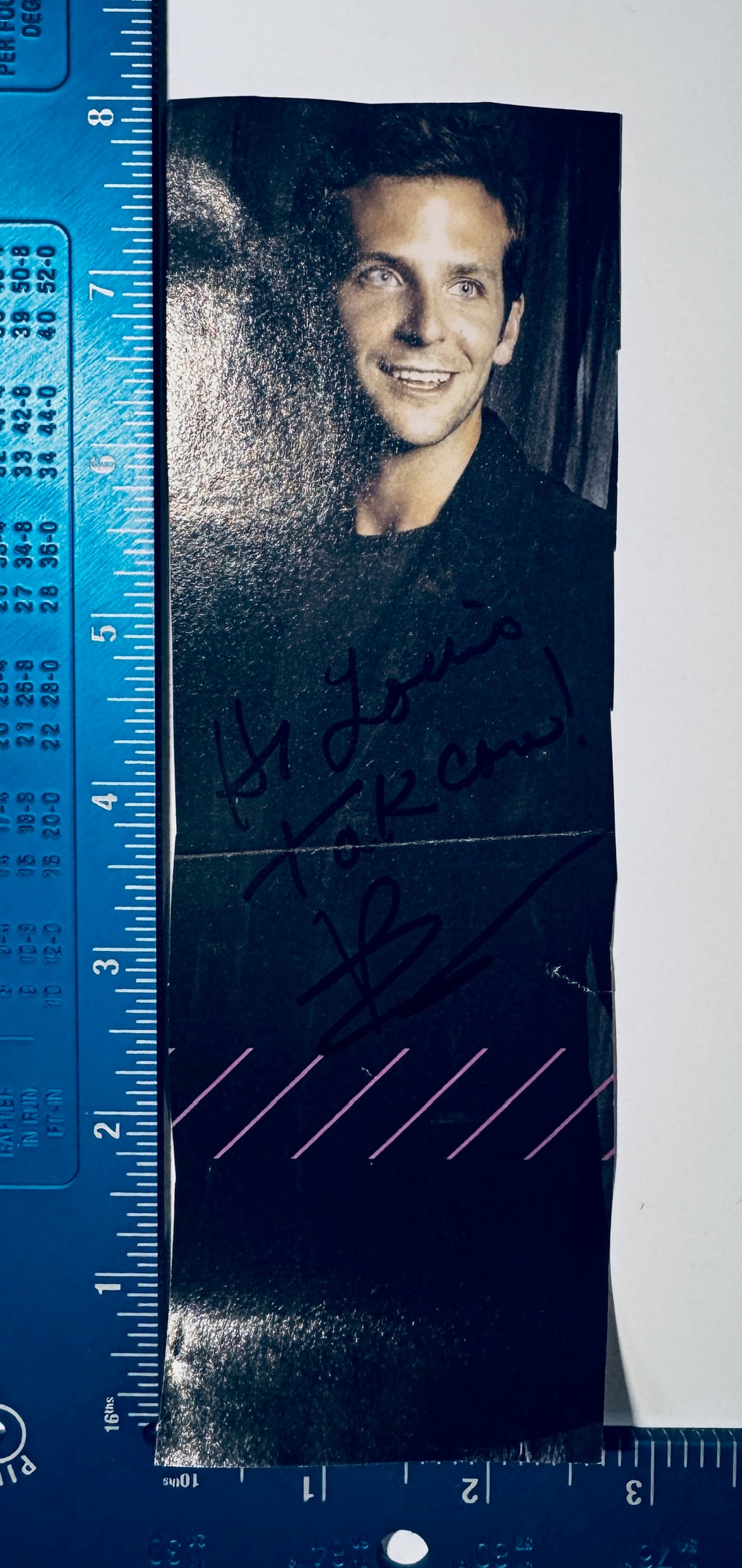 Bradley Cooper autographed magazine clipping shown next to a blue ruler measuring approximately 3 by 8 inches.