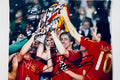 Autographed color photograph of Carles Puyol and Spain national team lifting the trophy hand-signed in black marker.