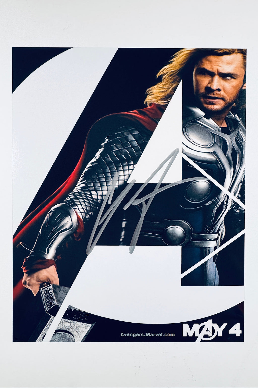 A promotional poster portrait of Chris Hemsworth as Thor from The Avengers, featuring the character's arm holding Mjolnir and a partial view of his face and armor, with a silver autograph signed across the center.