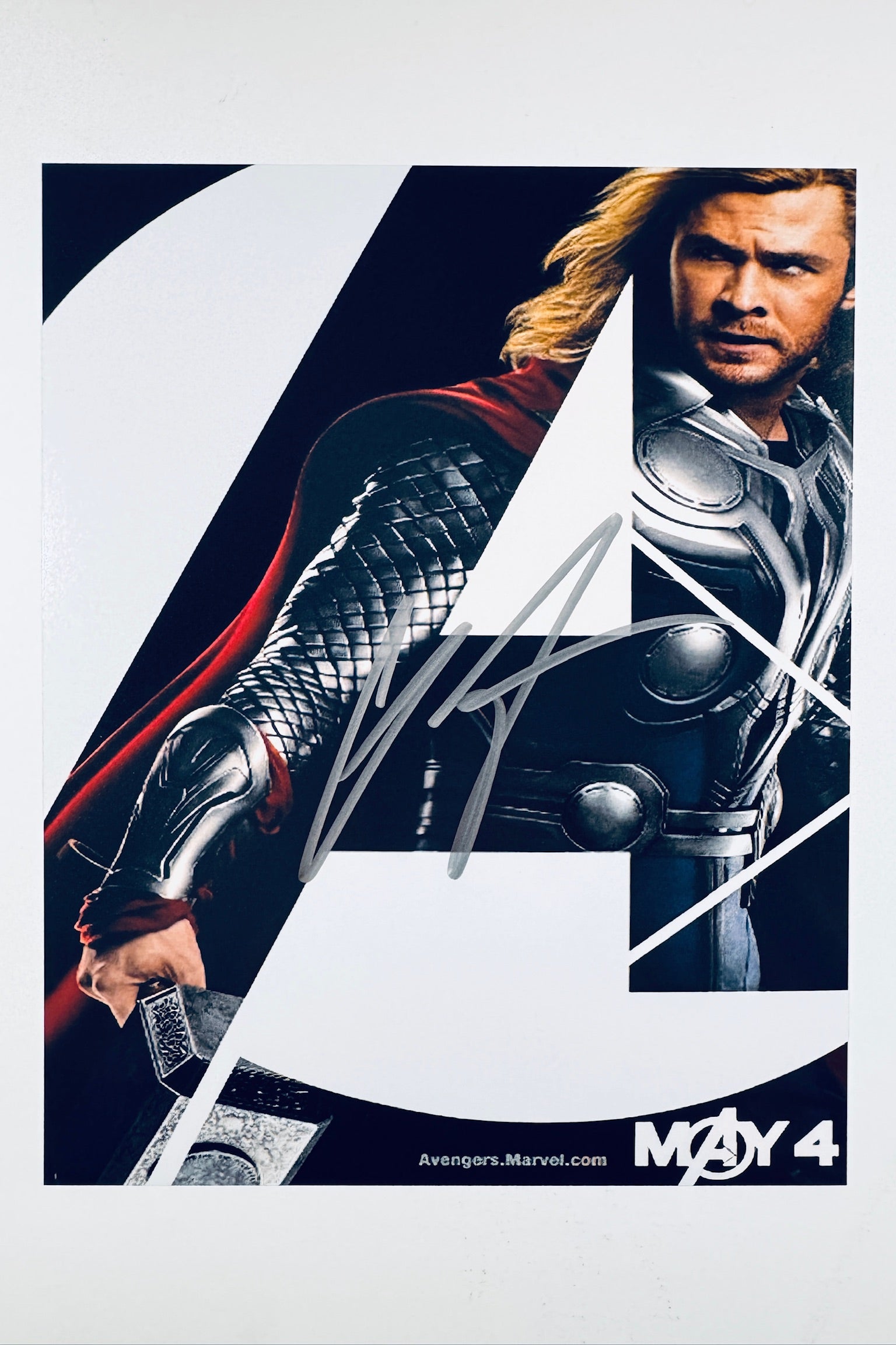 A promotional poster portrait of Chris Hemsworth as Thor from The Avengers, featuring the character's arm holding Mjolnir and a partial view of his face and armor, with a silver autograph signed across the center.