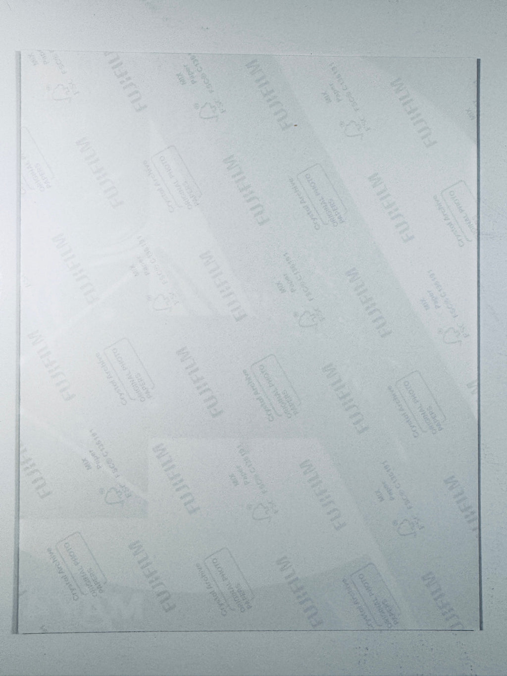 The plain white reverse side of a photographic print showing faint translucent watermark patterns and repeating Fujifilm paper logos.