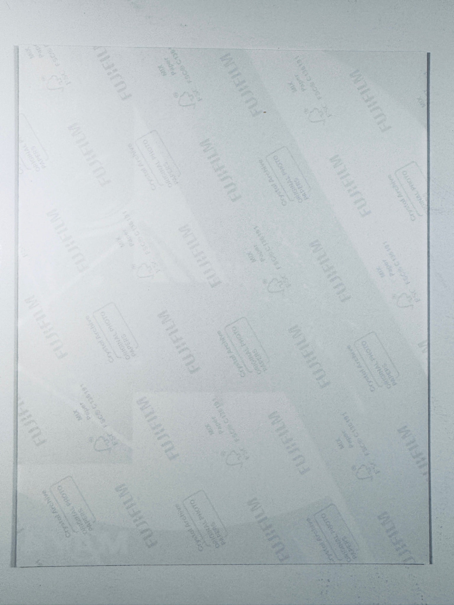 The plain white reverse side of a photographic print showing faint translucent watermark patterns and repeating Fujifilm paper logos.