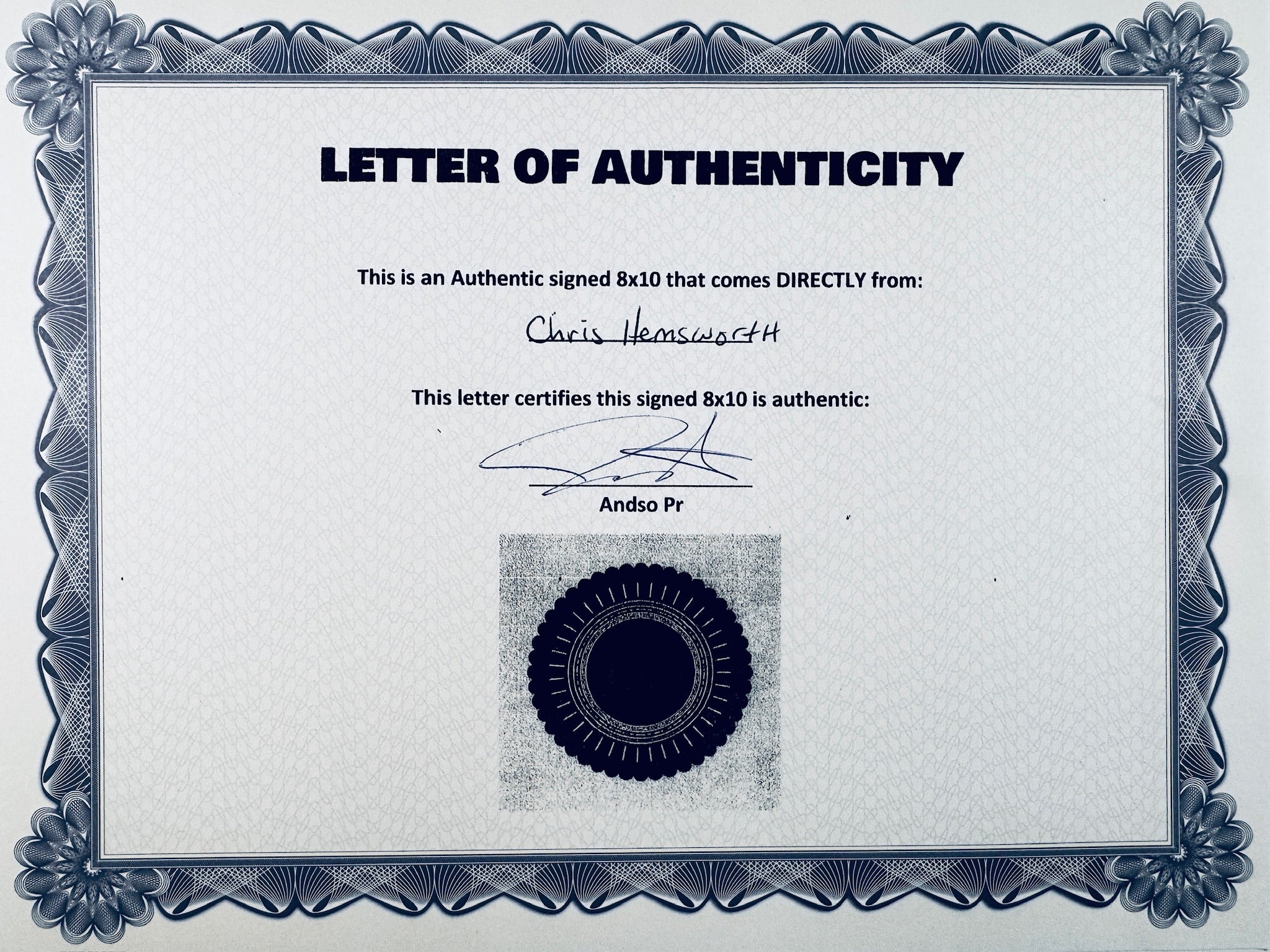 A Certificate of Authenticity featuring a decorative blue-patterned border, text certifying an authentic signed 8x10 from Chris Hemsworth, a signature, and a dark circular seal graphic at the bottom center.