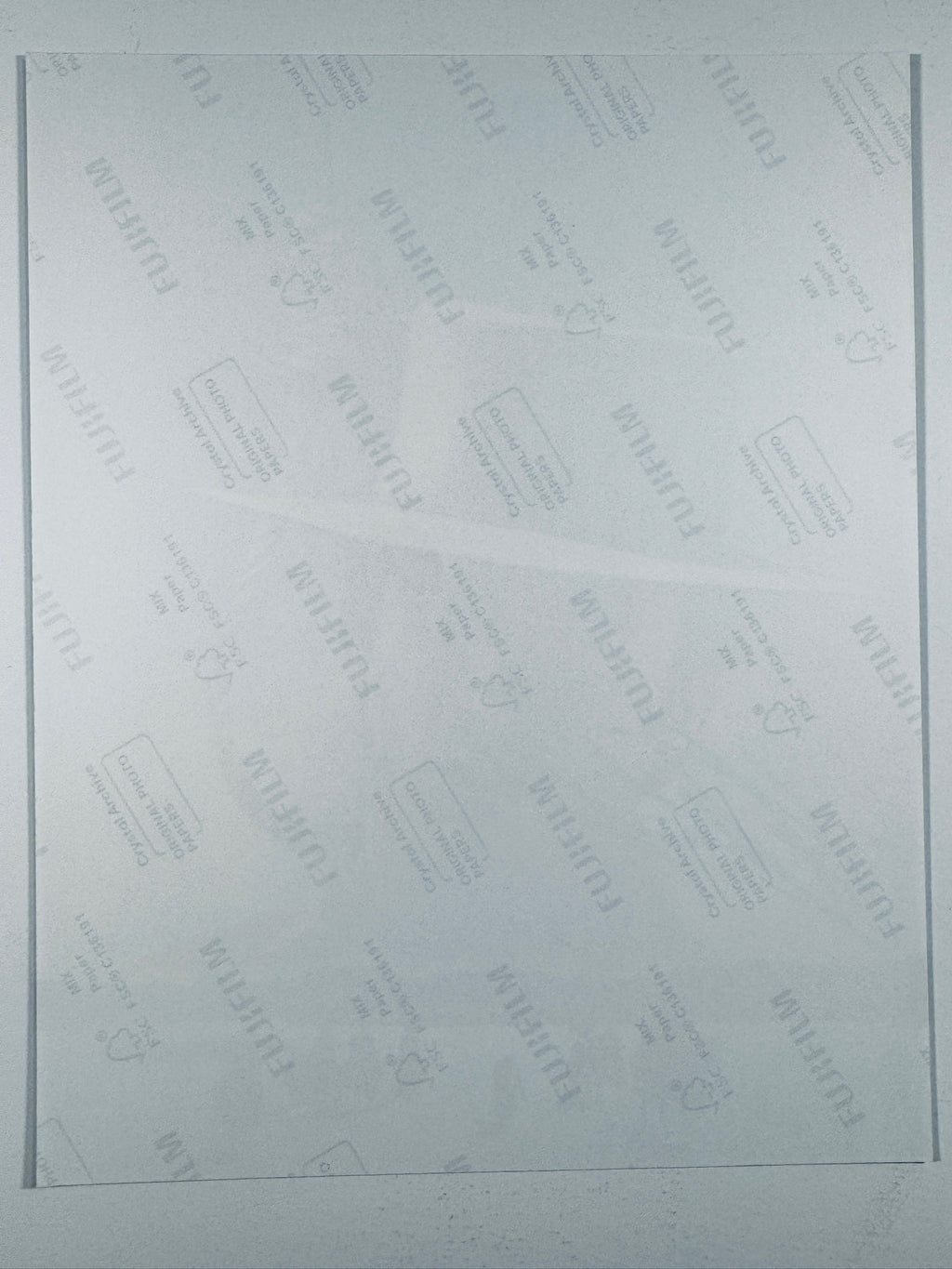 The plain white reverse side of a photographic print showing faint translucent watermark patterns and repeating Fujifilm paper logos.