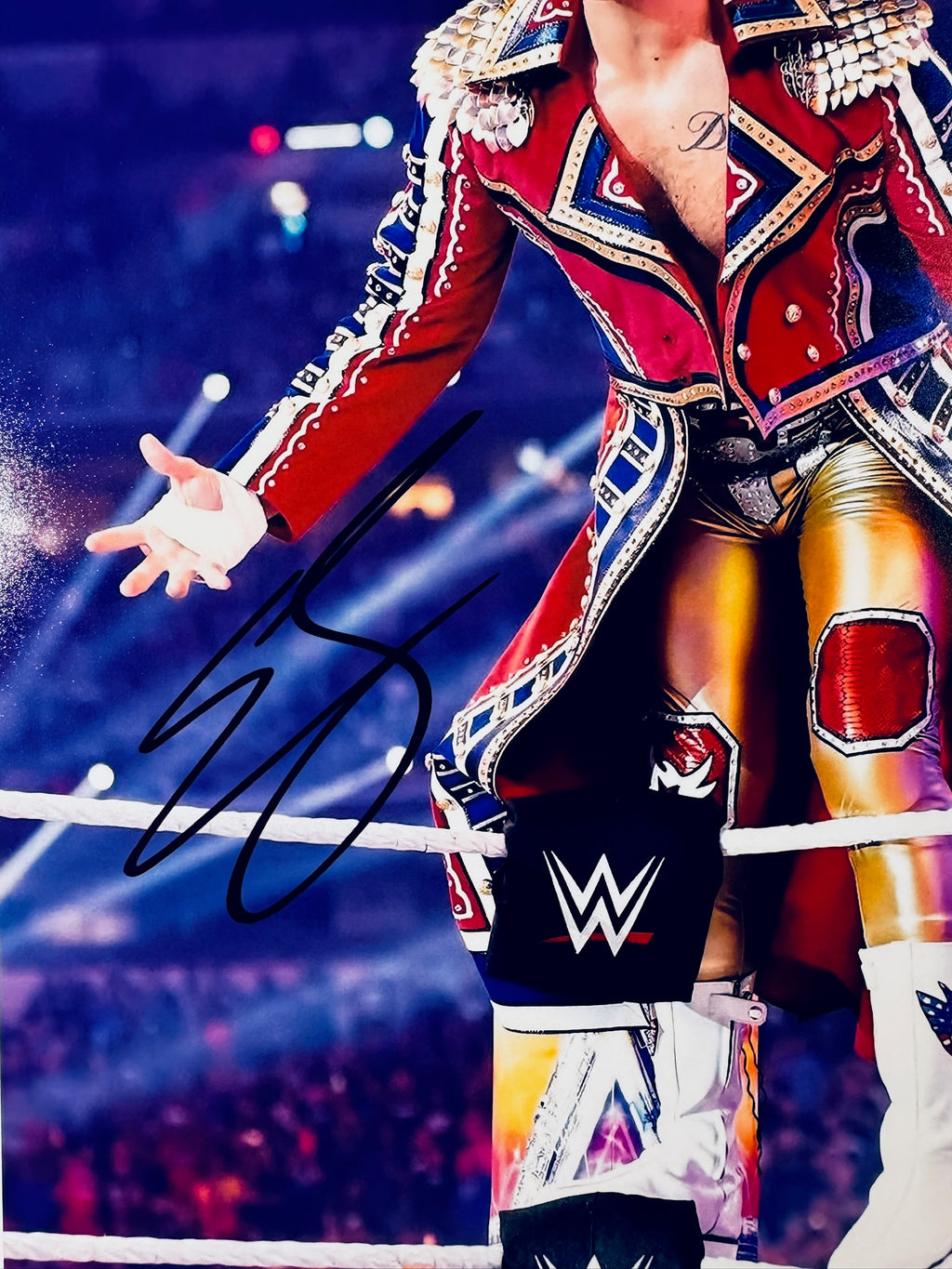 Close-up view of Cody Rhodes's black autograph across the ring ropes and his red coat on the promotional photograph.