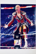 Signed full photo of Cody Rhodes standing on a ring turnbuckle in a red and blue ornate coat and gold wrestling gear, featuring a black autograph.