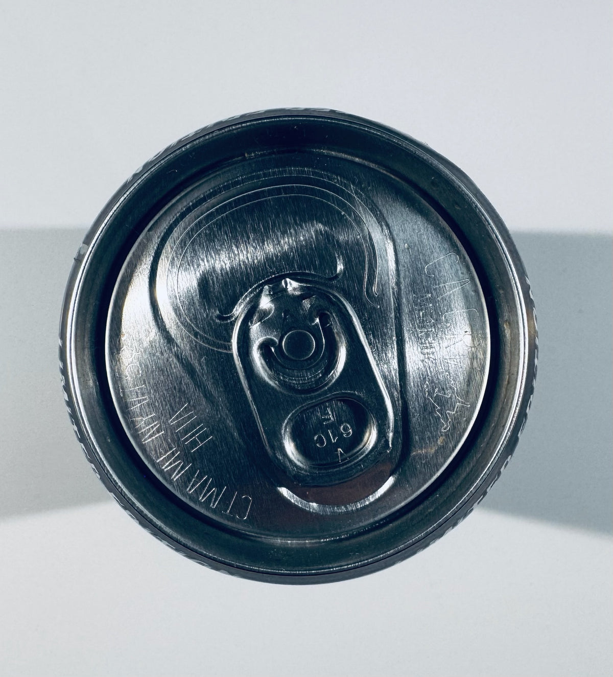 Top-down view of a dark metallic beverage can lid with a pull-tab opening, photographed against a light gray background.