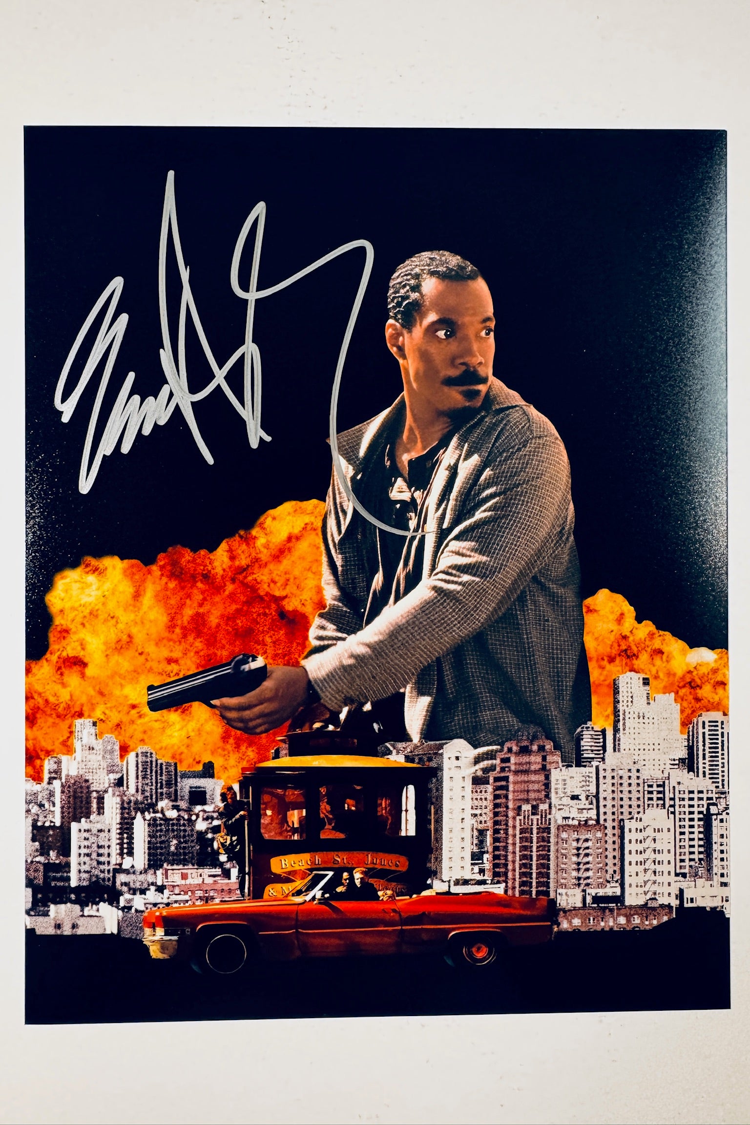 Eddie Murphy hand-signed 8x10 action photo from the movie Metro, holding a gun with a city skyline, explosion background, and red car.