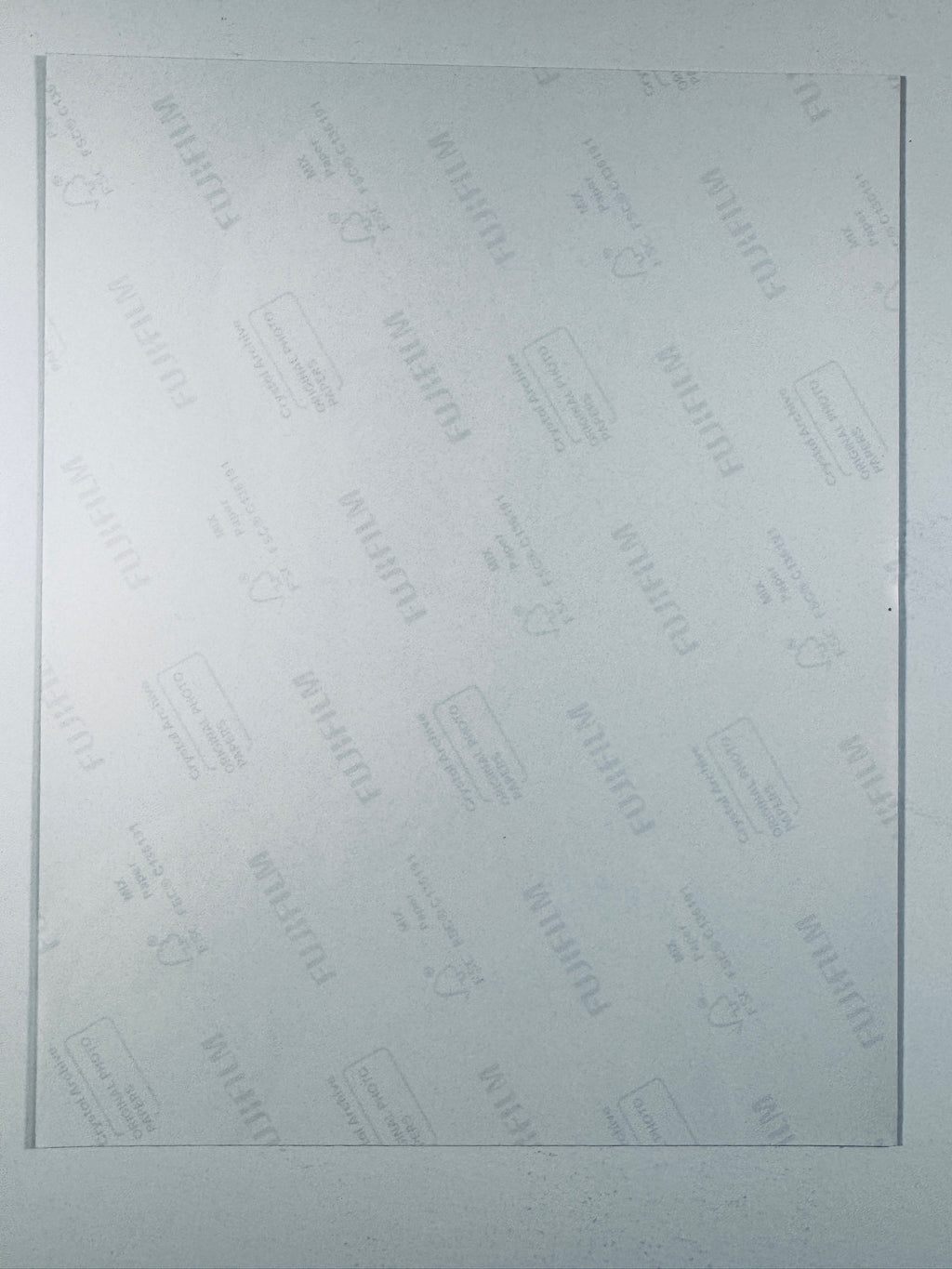 The plain white reverse side of a photographic print showing faint translucent watermark patterns and repeating Fujifilm paper logos.