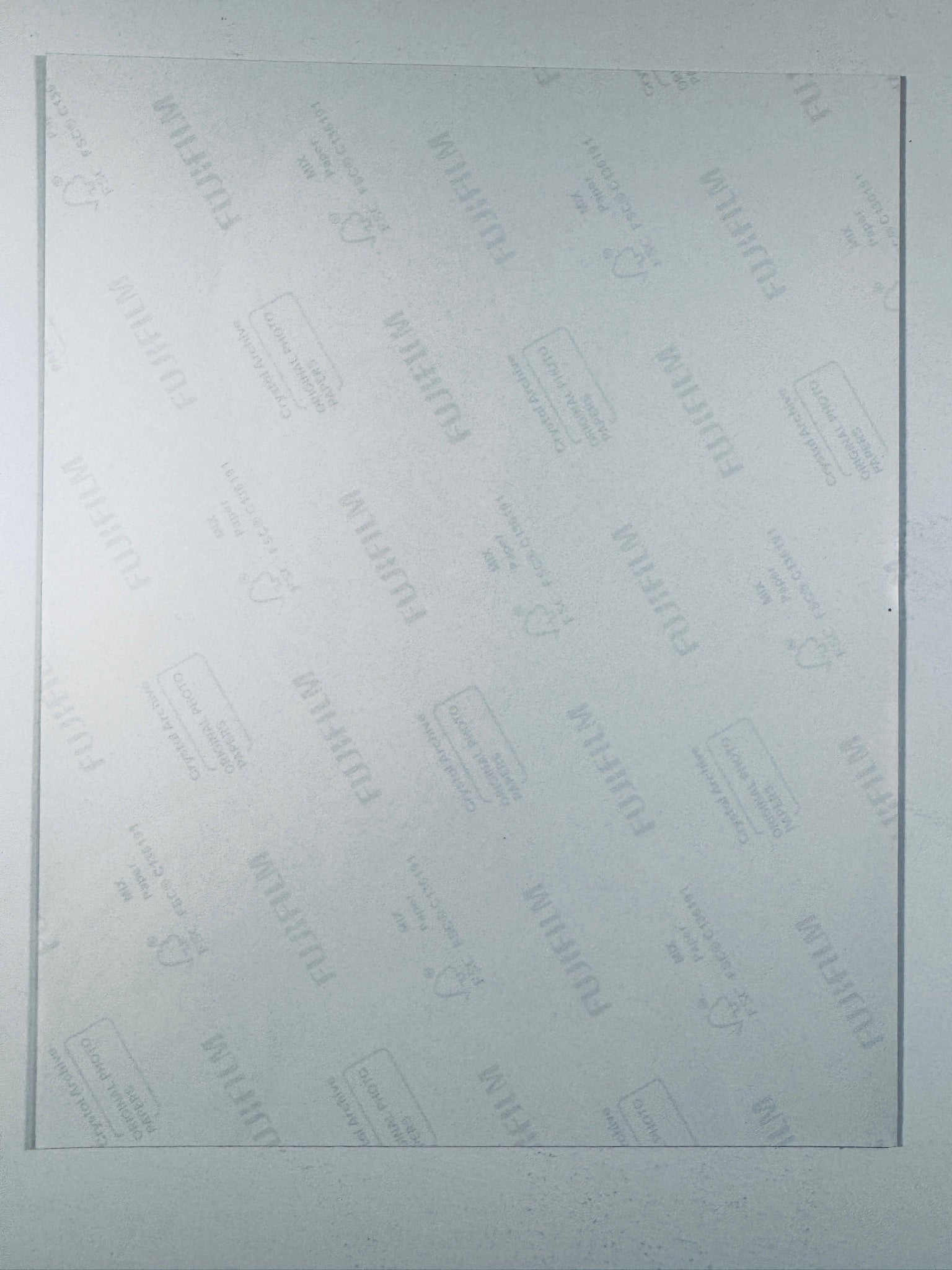 The plain white reverse side of a photographic print showing faint translucent watermark patterns and repeating Fujifilm paper logos.