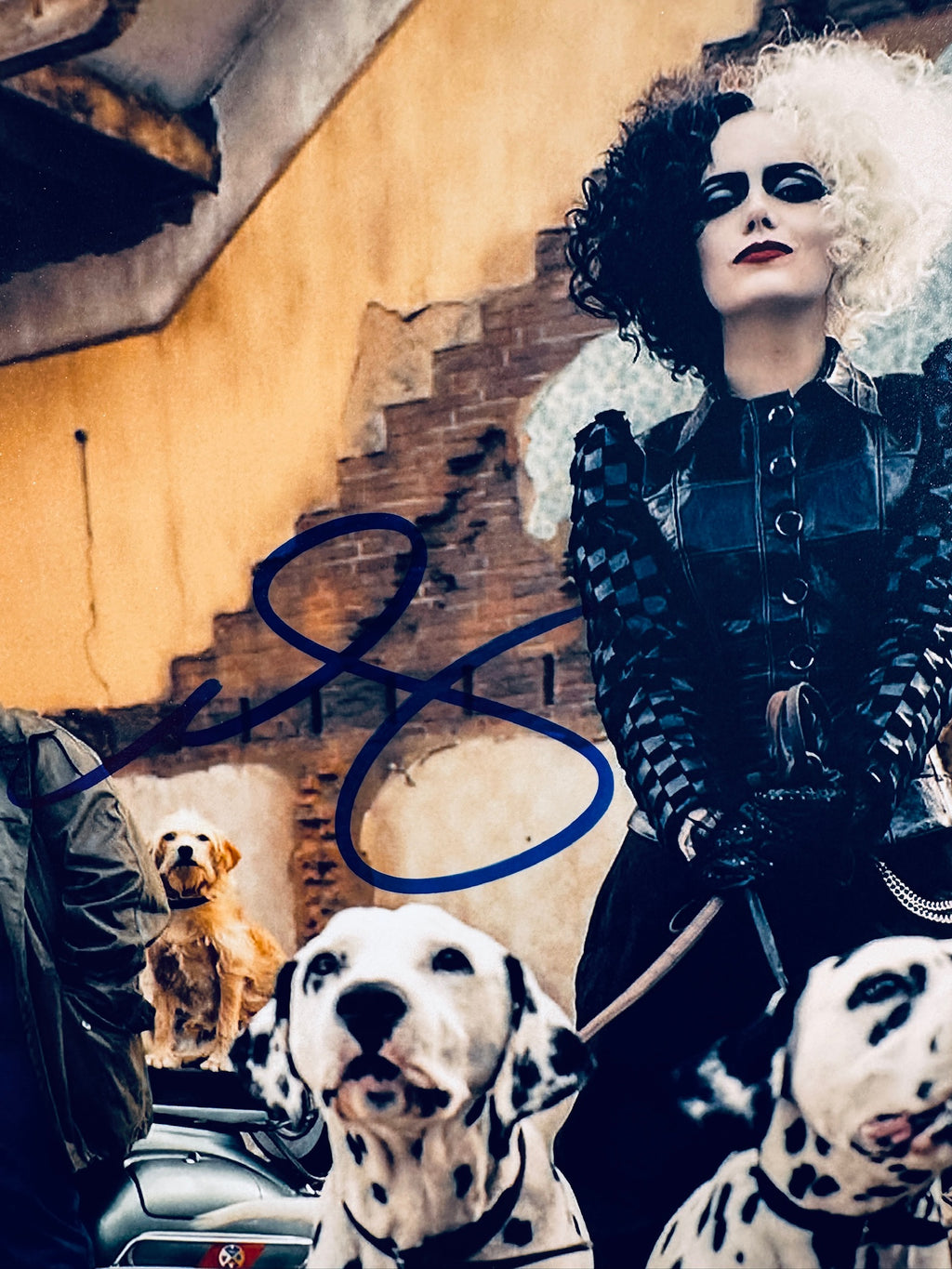 Close-up view of Emma Stone's signature in blue marker across the Cruella promotional matte photo.