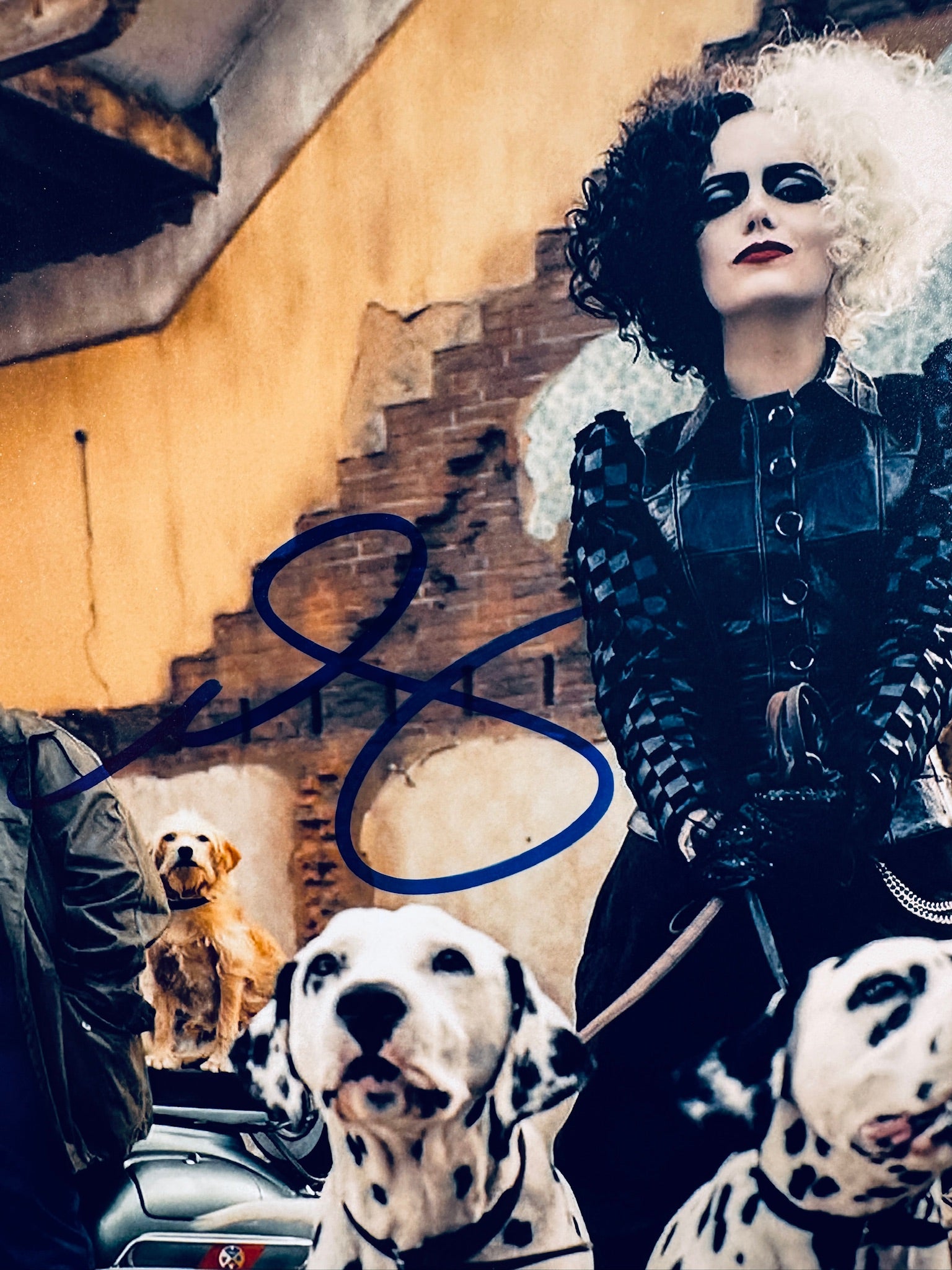 Close-up view of Emma Stone's signature in blue marker across the Cruella promotional matte photo.