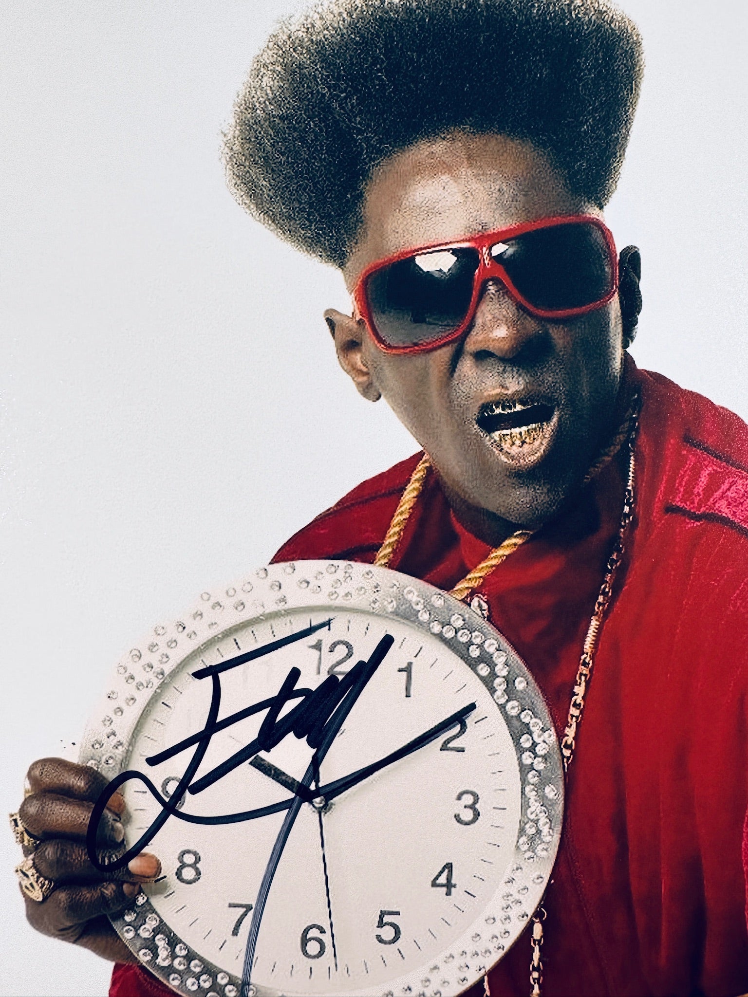 Close-up view of Flavor Flav's signature in black marker across the white face of the clock in the promotional photo.