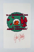 A white printed card featuring a Christmas wreath illustration with the text 'TO ALL HEATHCLIFF'S FANS A VERY MERRY CHRISTMAS!' and a red signature reading 'Geo Gently' below, photographed against a light gray background.