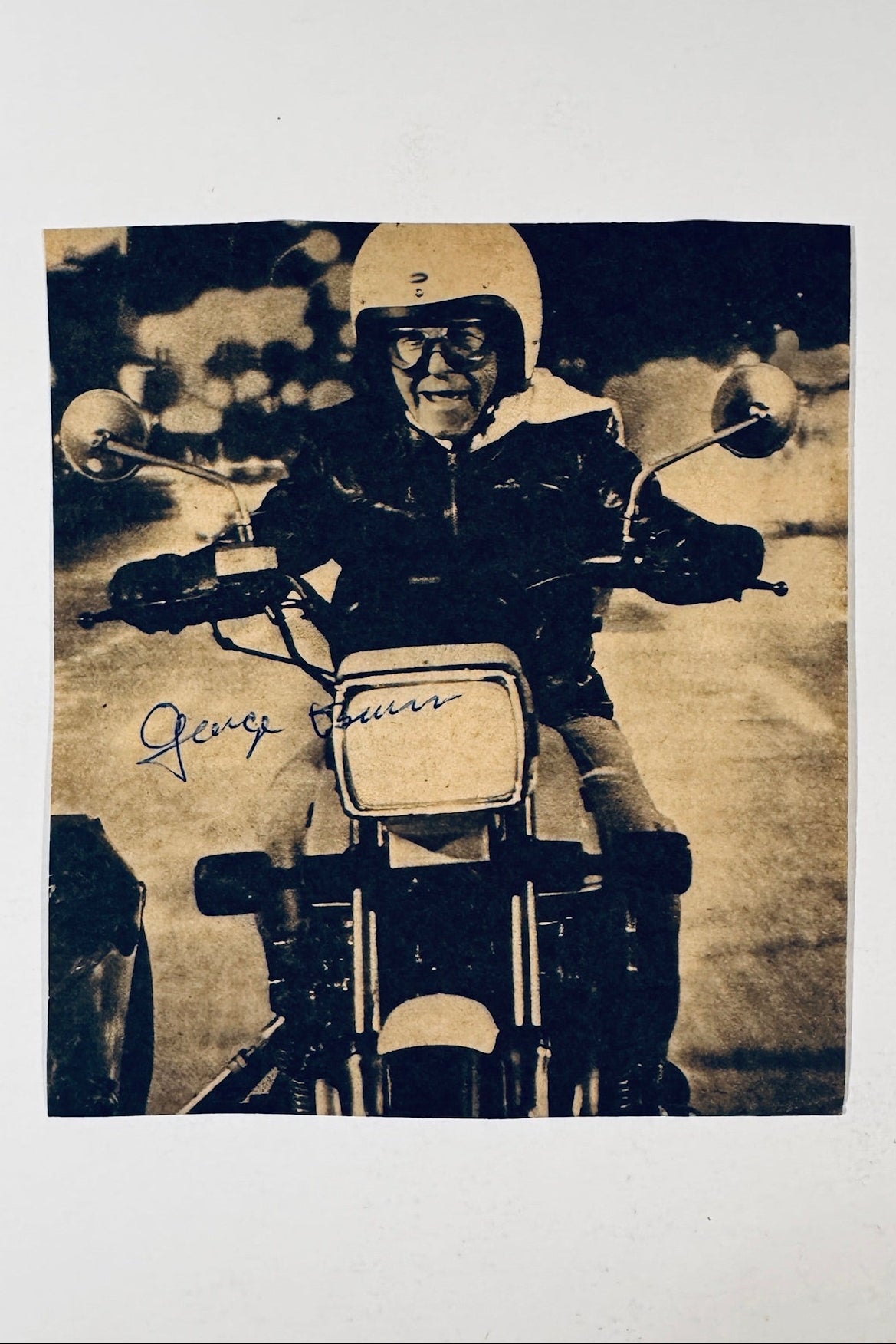 George Burns autographed photo riding a motorcycle in helmet and goggles signed in blue ink.