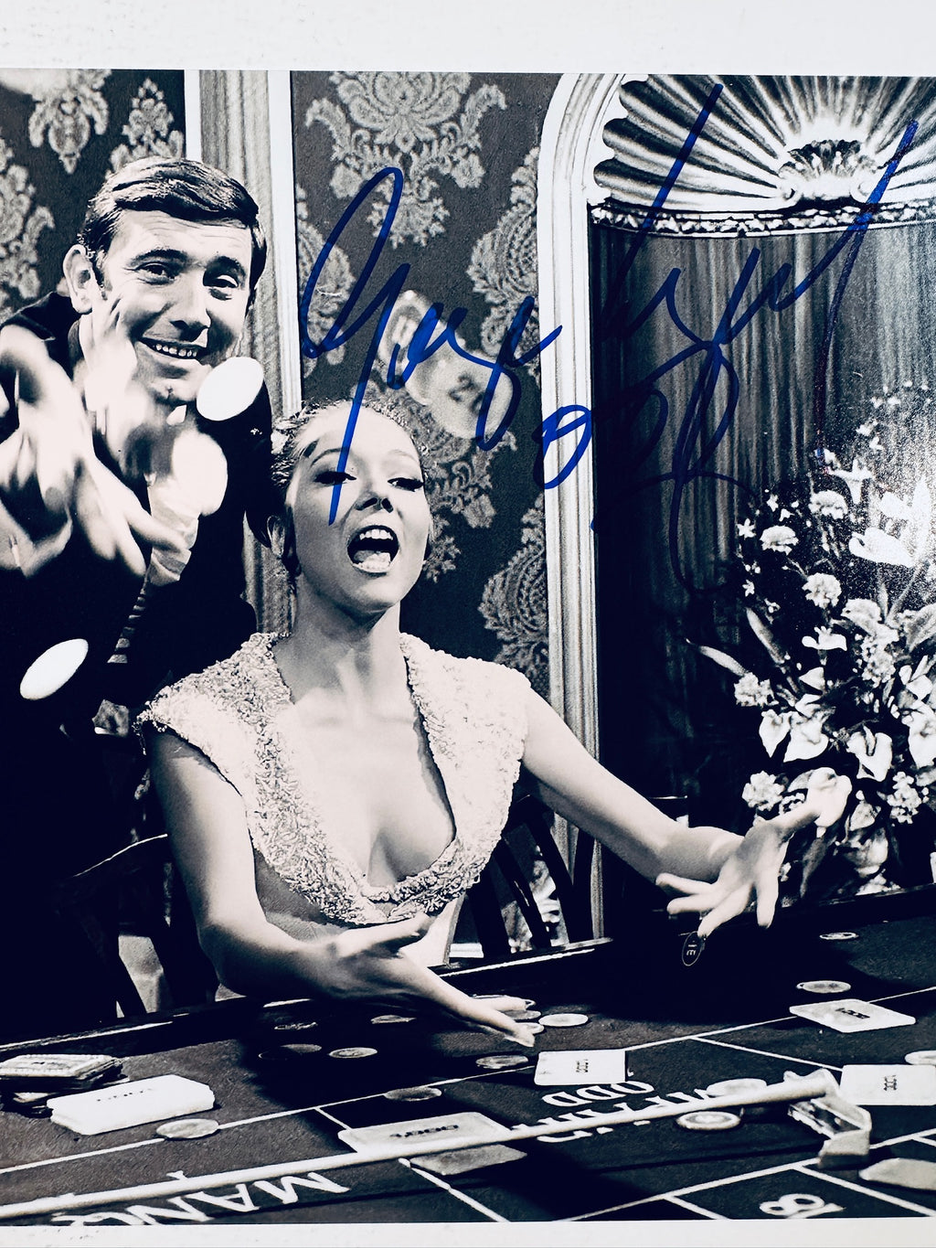 Close-up view of George Lazenby and Diana Rigg's signatures in blue marker across the vintage James Bond matte photo.
