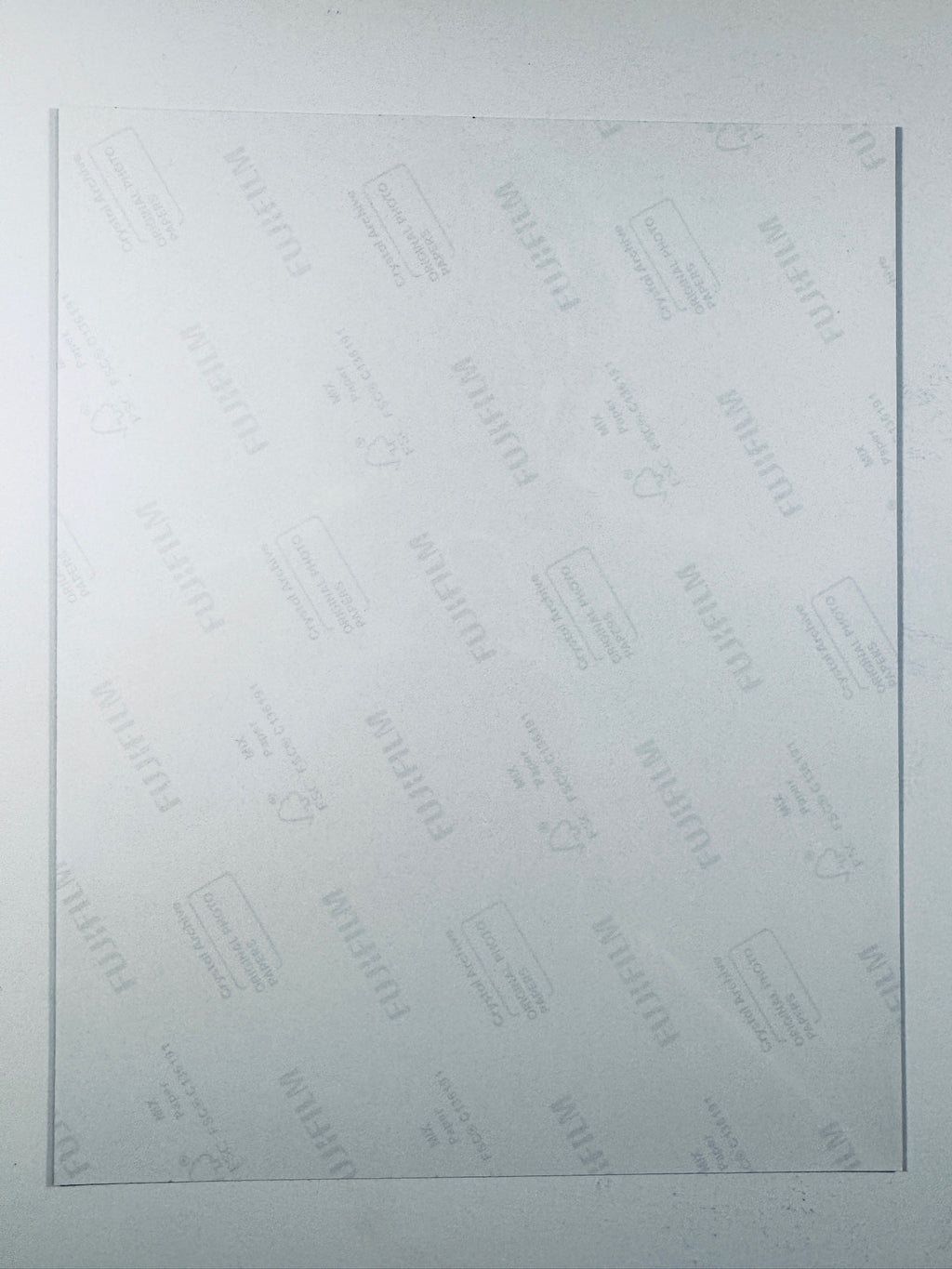 The plain white reverse side of a photographic print showing faint translucent watermark patterns and repeating Fujifilm paper logos.
