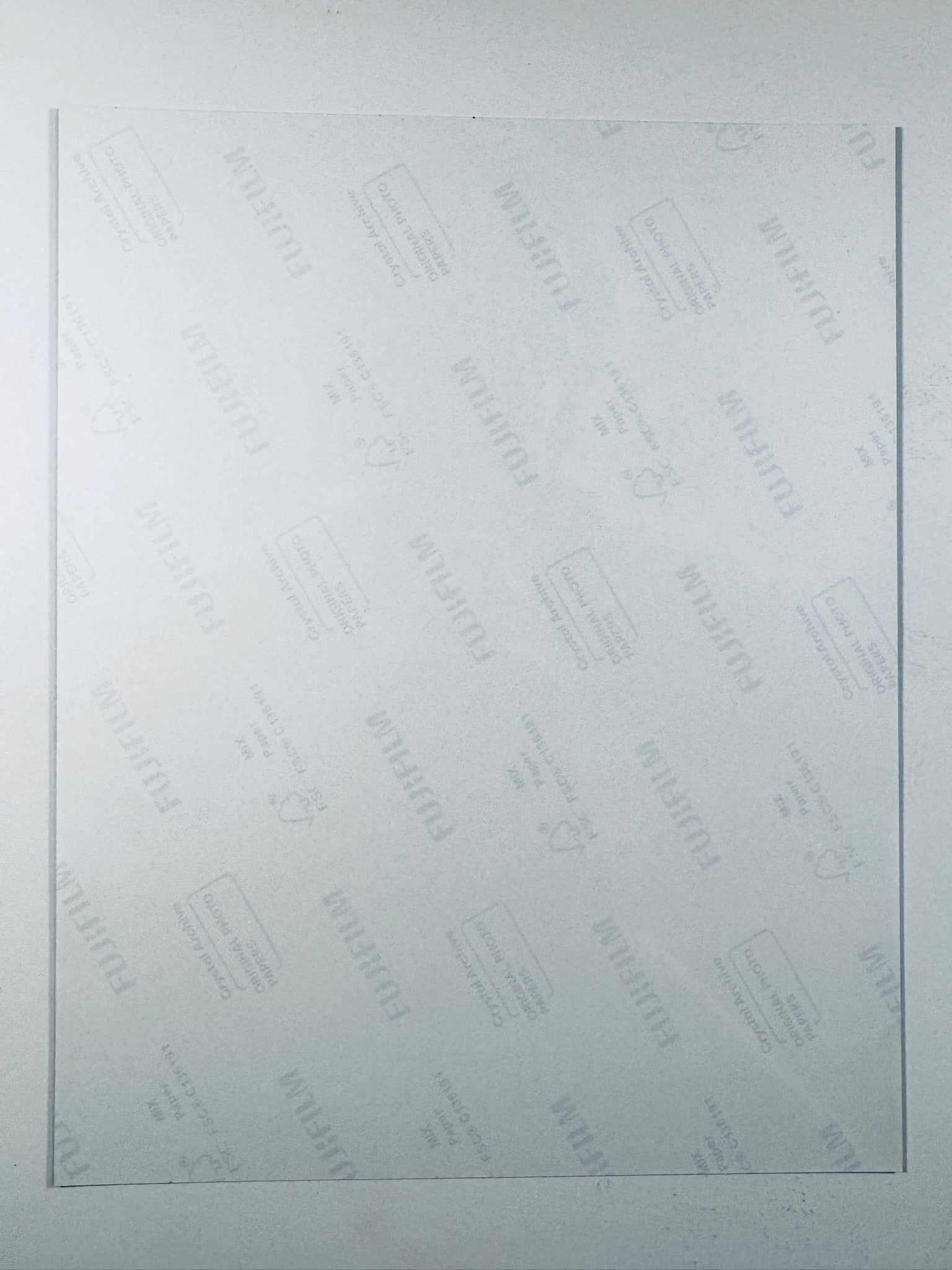 The plain white reverse side of a photographic print showing faint translucent watermark patterns and repeating Fujifilm paper logos.