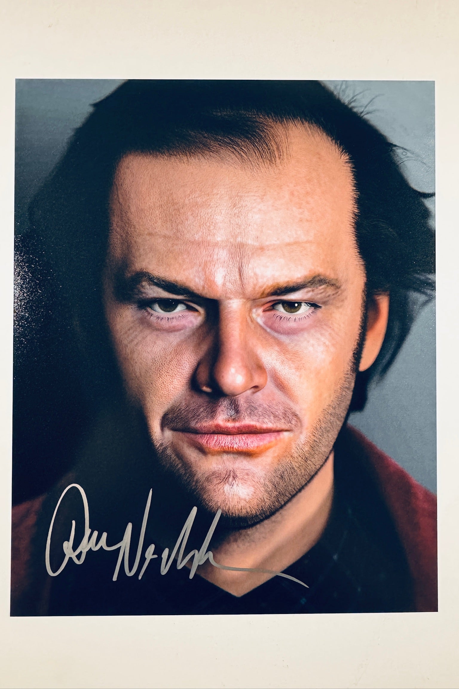 A close-up portrait of Jack Nicholson as Jack Torrance from The Shining with an intense expression, featuring a signature in light-colored ink on the lower left.