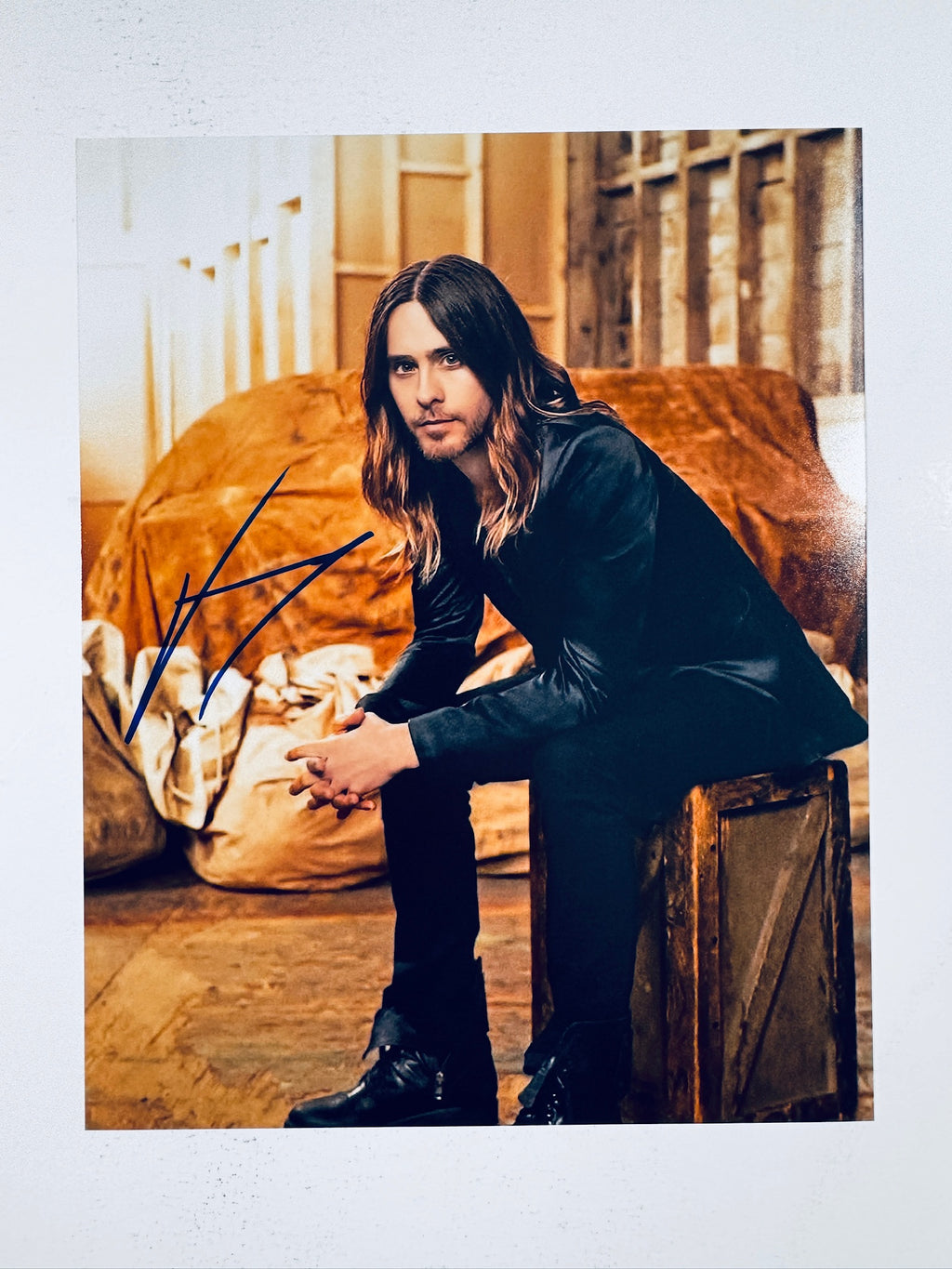 Signed 8x10 matte portrait of actor and musician Jared Leto sitting on a wooden crate with long hair and a beard, featuring a bold blue ink autograph on the left.