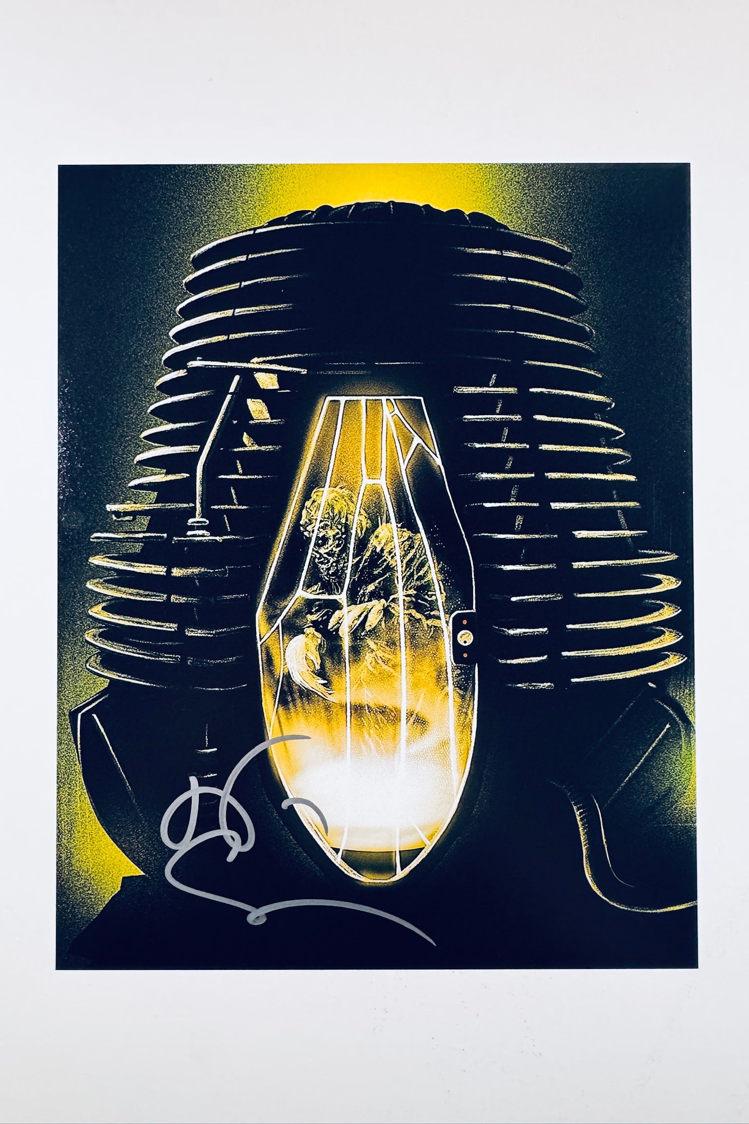 An illustrative, stylized art print depicting a human figure trapped inside a glowing telepod capsule with ribbed machine elements in the background, featuring a grey/silver autograph signed across the lower left area.