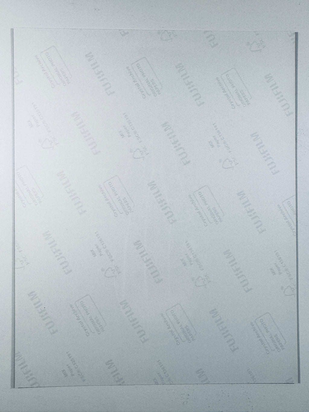The plain white reverse side of a photographic print showing faint translucent watermark patterns and repeating Fujifilm paper logos.