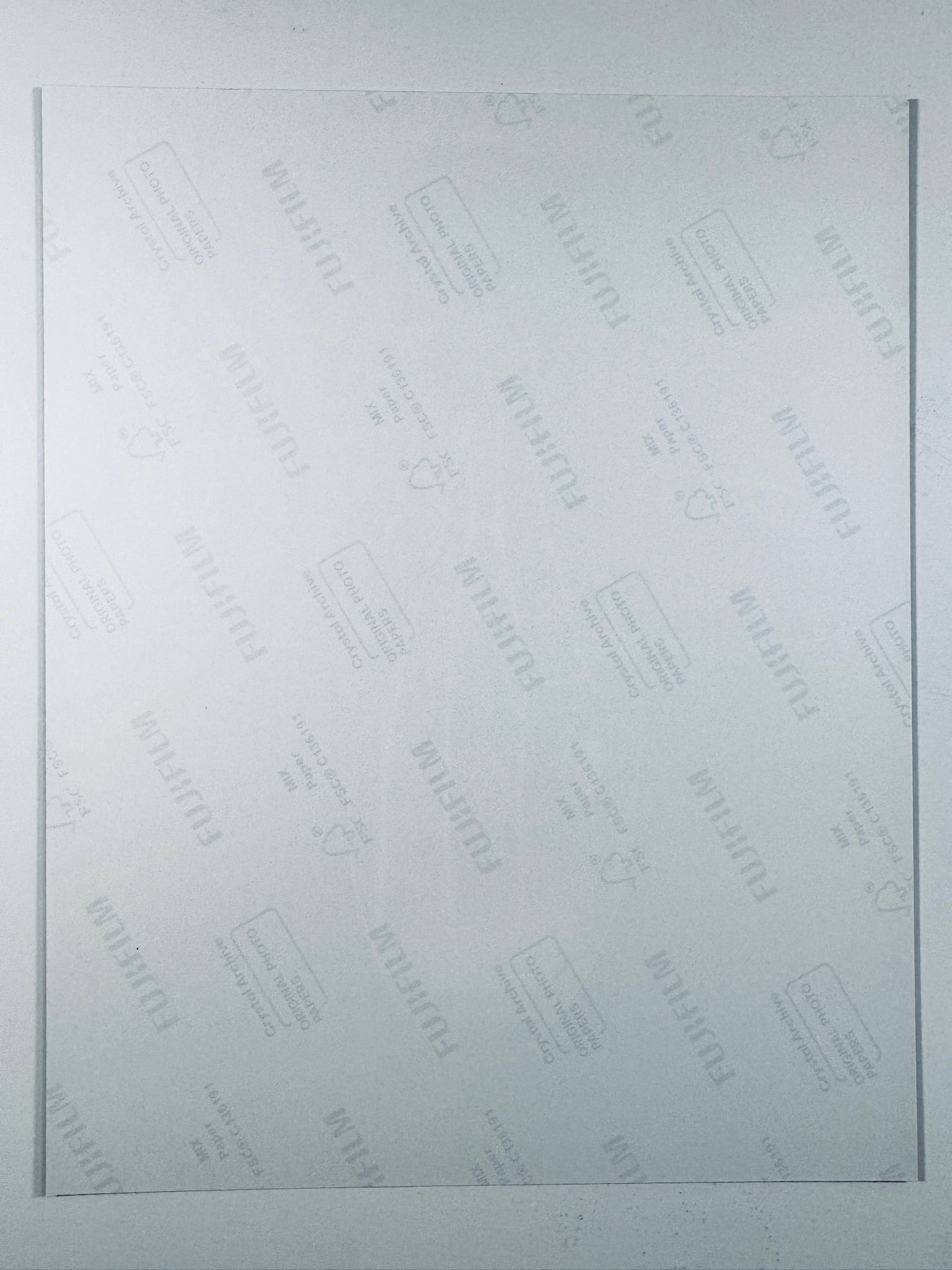 The plain white reverse side of a photographic print showing faint translucent watermark patterns and repeating Fujifilm paper logos.
