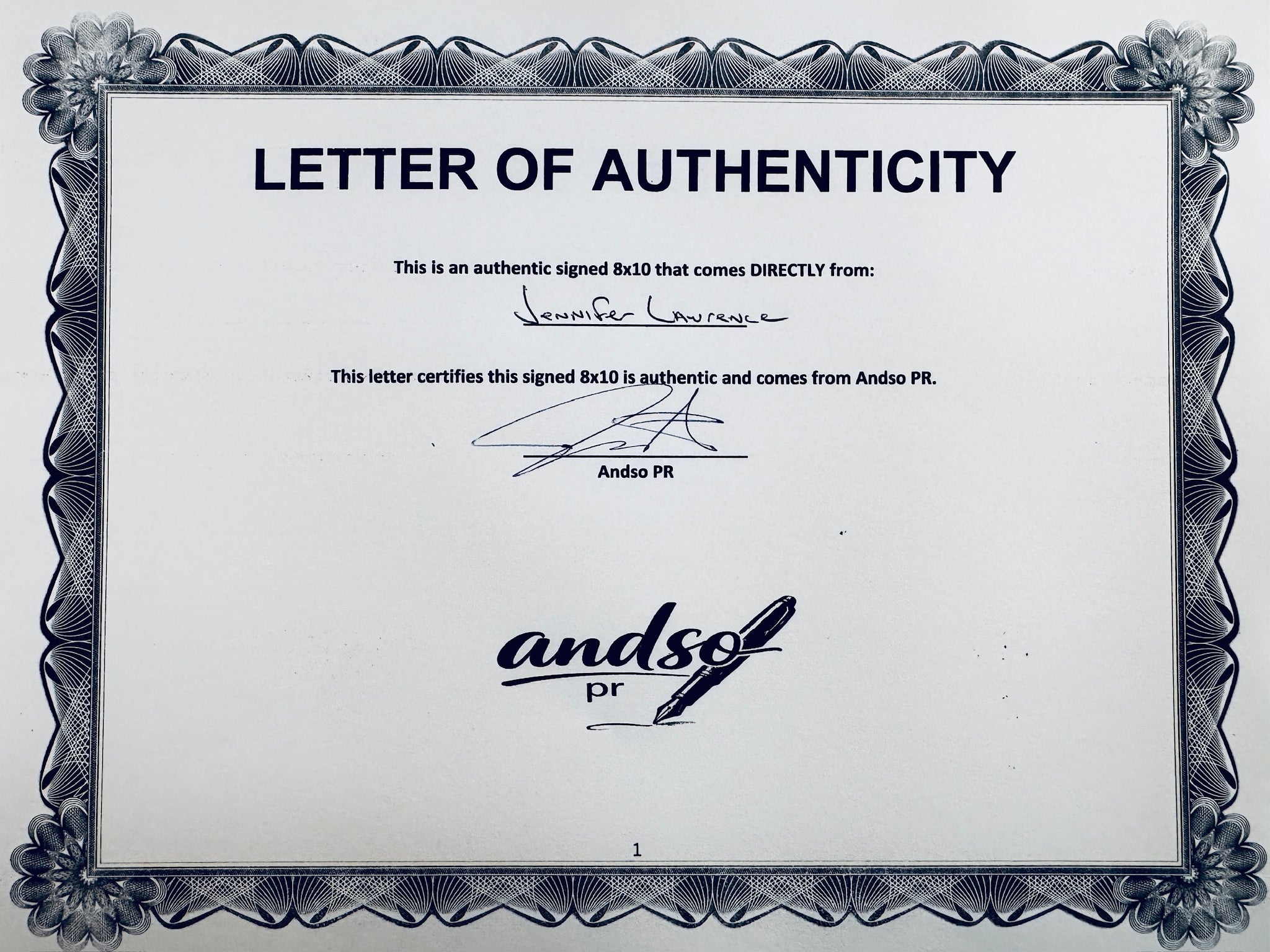 A Letter of Authenticity with a decorative blue-patterned border for The Hunger Games: Catching Fire signed 8x10, certifying an authentic autograph coming directly from Jennifer Lawrence, featuring a signature at the top.