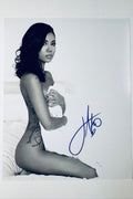Signed full photo of Jhene Aiko posing kneeling on a bed while wrapped in a white sheet, featuring a blue autograph.