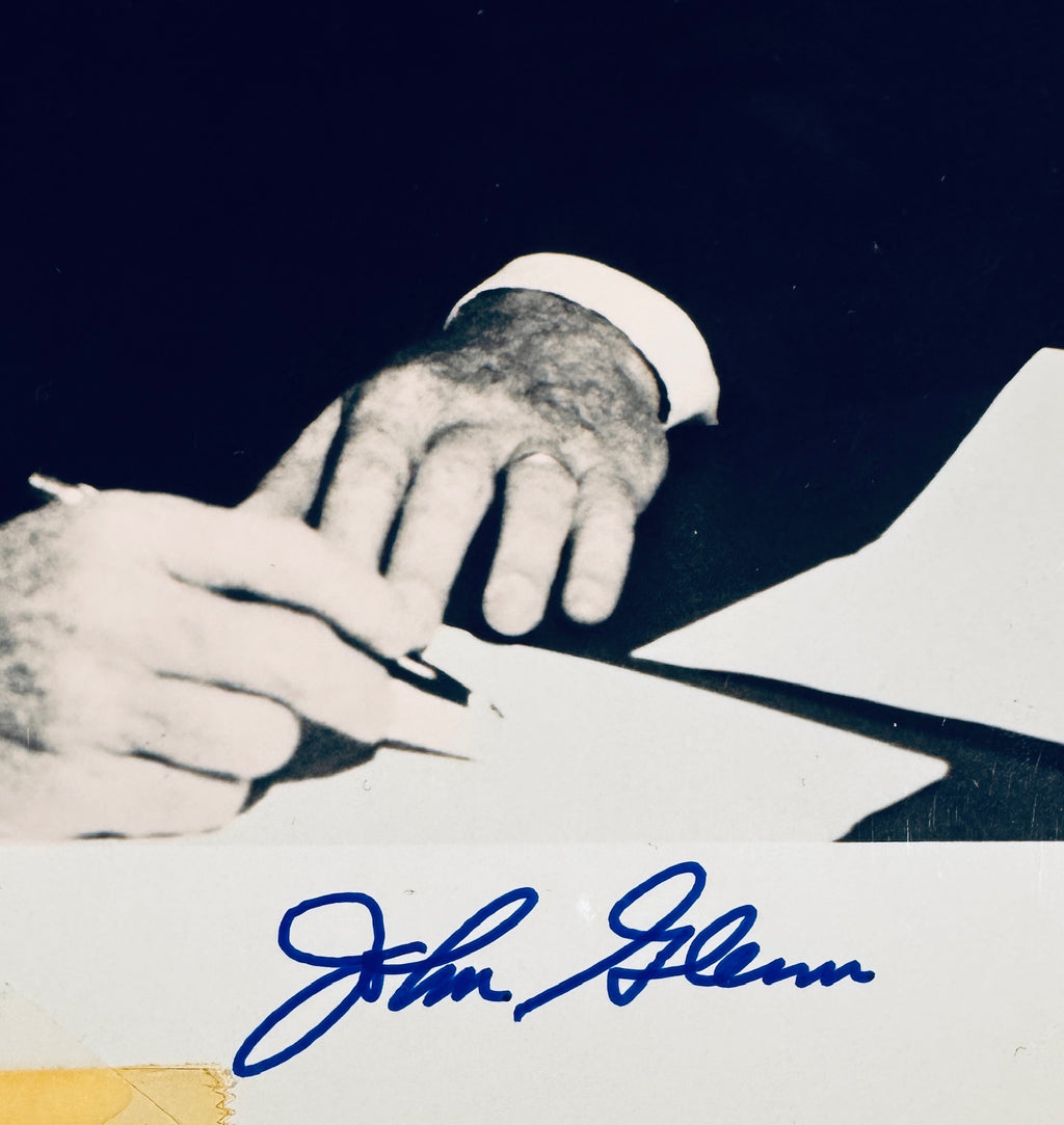 Close-up view of John Glenn autograph signature in blue pen on the bottom border of the photo.