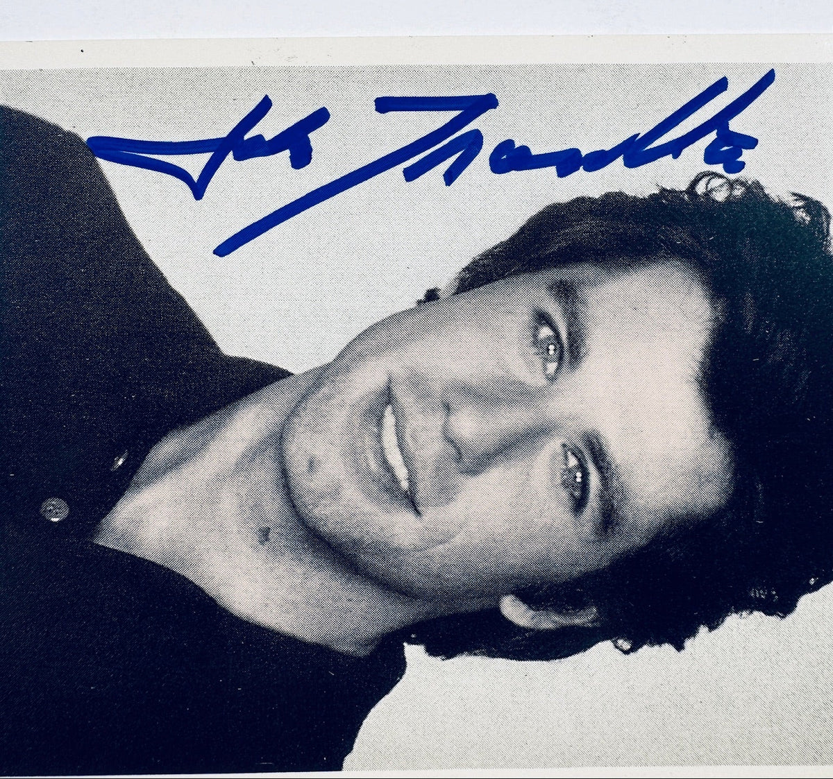 Close-up detail of John Travolta signature in blue felt-tip marker along photo margin.