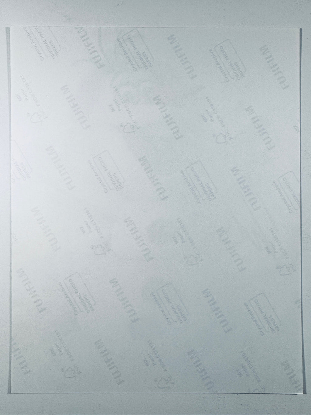 The plain white reverse side of a photographic print showing faint translucent watermark patterns and repeating Fujifilm paper logos.