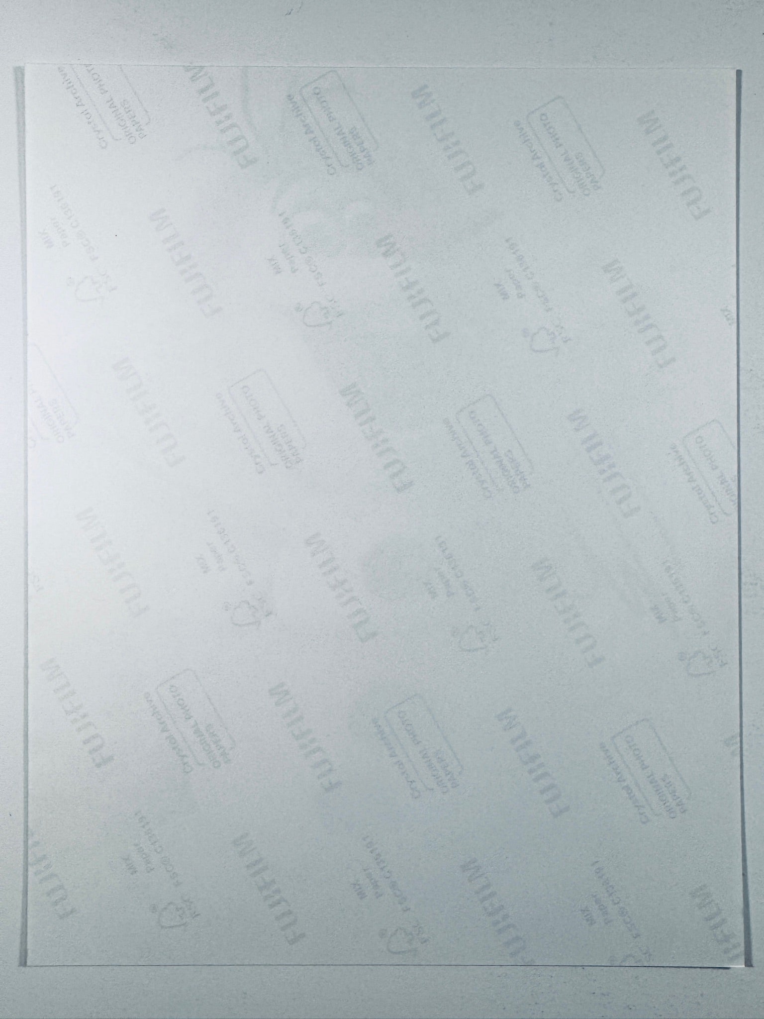 The plain white reverse side of a photographic print showing faint translucent watermark patterns and repeating Fujifilm paper logos.