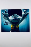 A still featuring Branch from Trolls holding his hands up making rock-on hand signs against a blue background, signed in black marker on the left side.