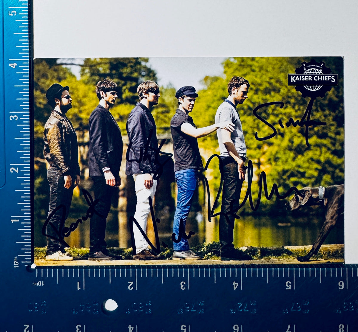 Full front view of autographed Kaiser Chiefs postcard with L-shaped ruler showing 4x6 inch measurements.