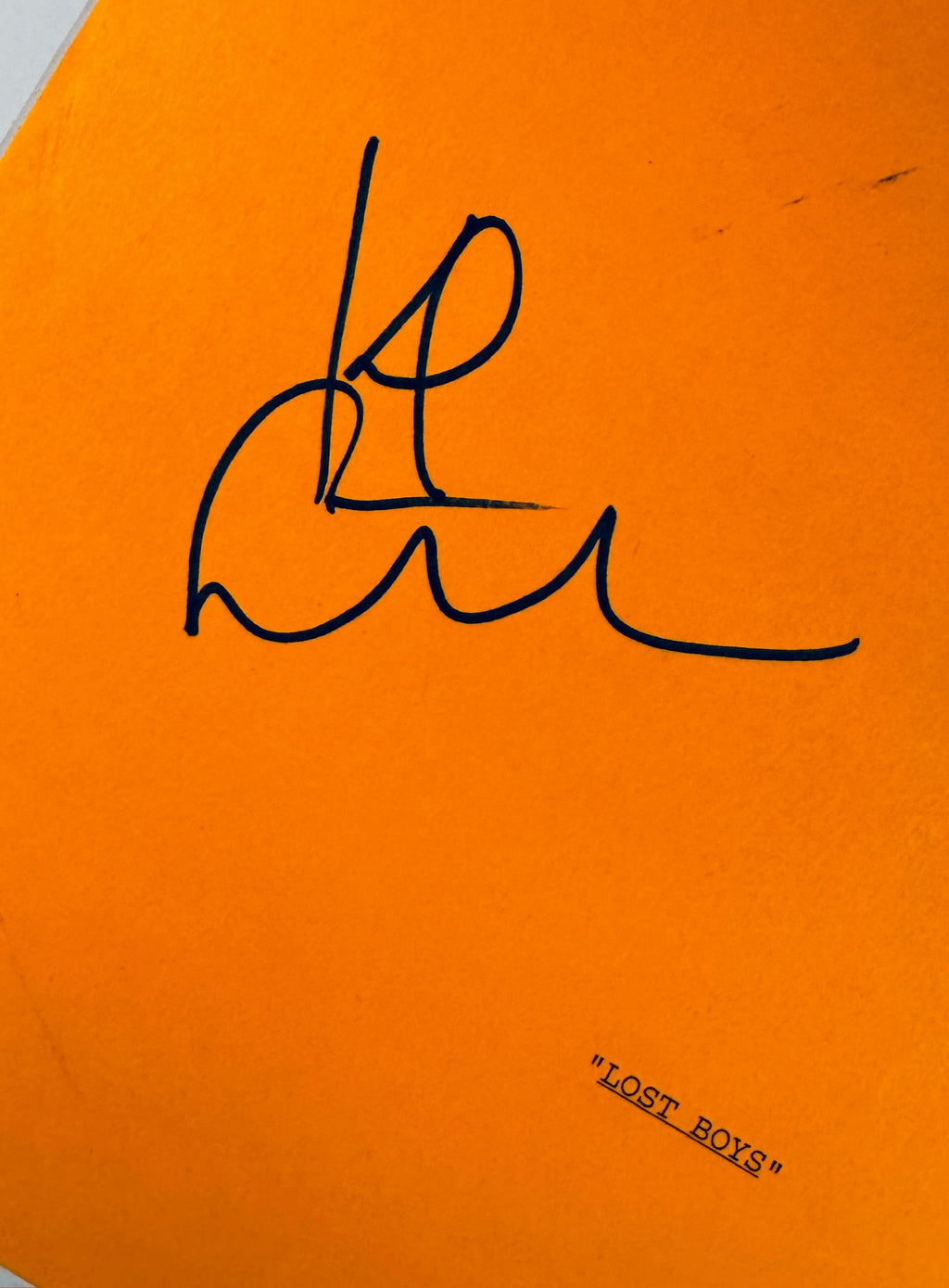 Close-up view of Kiefer Sutherland autograph signature in black marker on orange script cardstock.