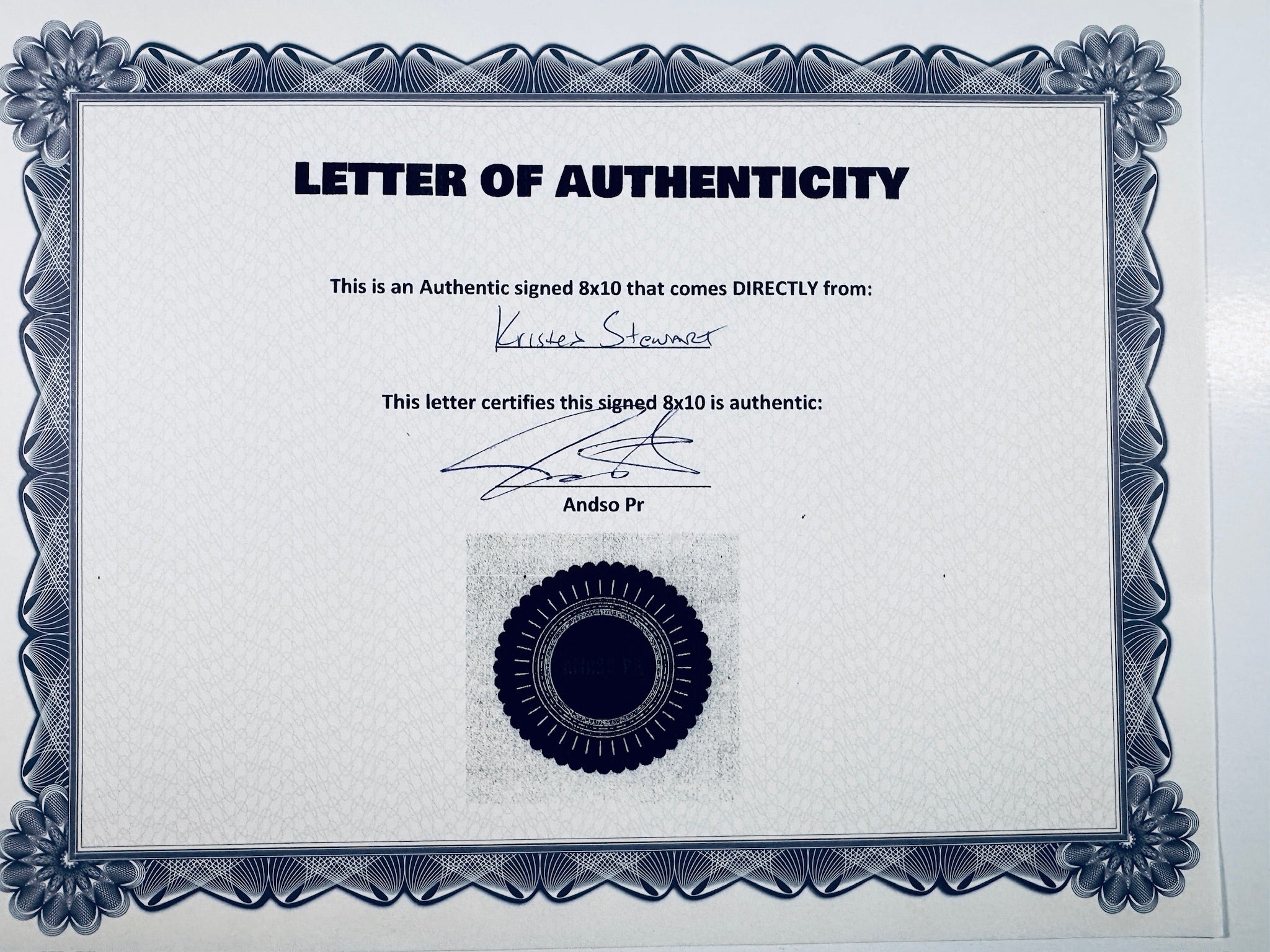 A Letter of Authenticity with a decorative blue-patterned border, certifying an authentic signed 8x10 coming directly from Kristen Stewart, featuring a dark circular seal graphic at the bottom.