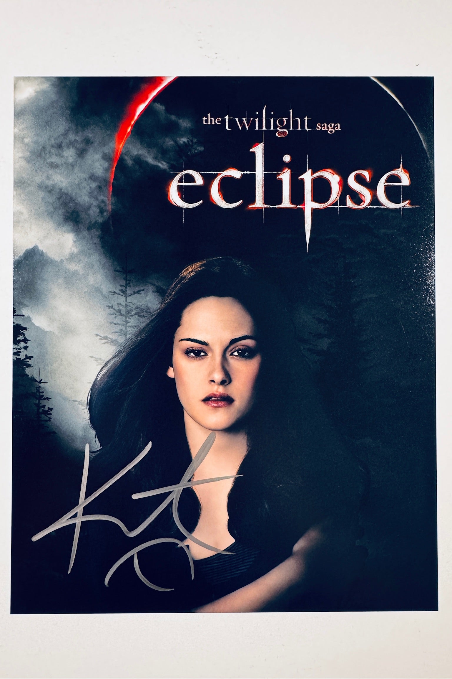 A promotional poster portrait for The Twilight Saga: Eclipse featuring Kristen Stewart as Bella Swan with dark hair against a moody forest background, with a silver marker signature across the lower portion.