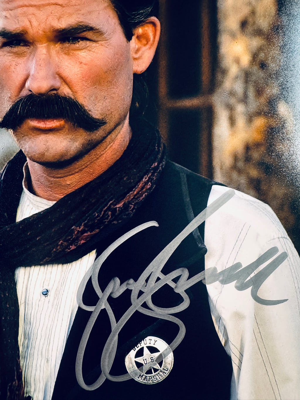 Close-up view of Kurt Russell's signature in silver marker on his Tombstone promotional photo next to the Deputy Marshal badge.