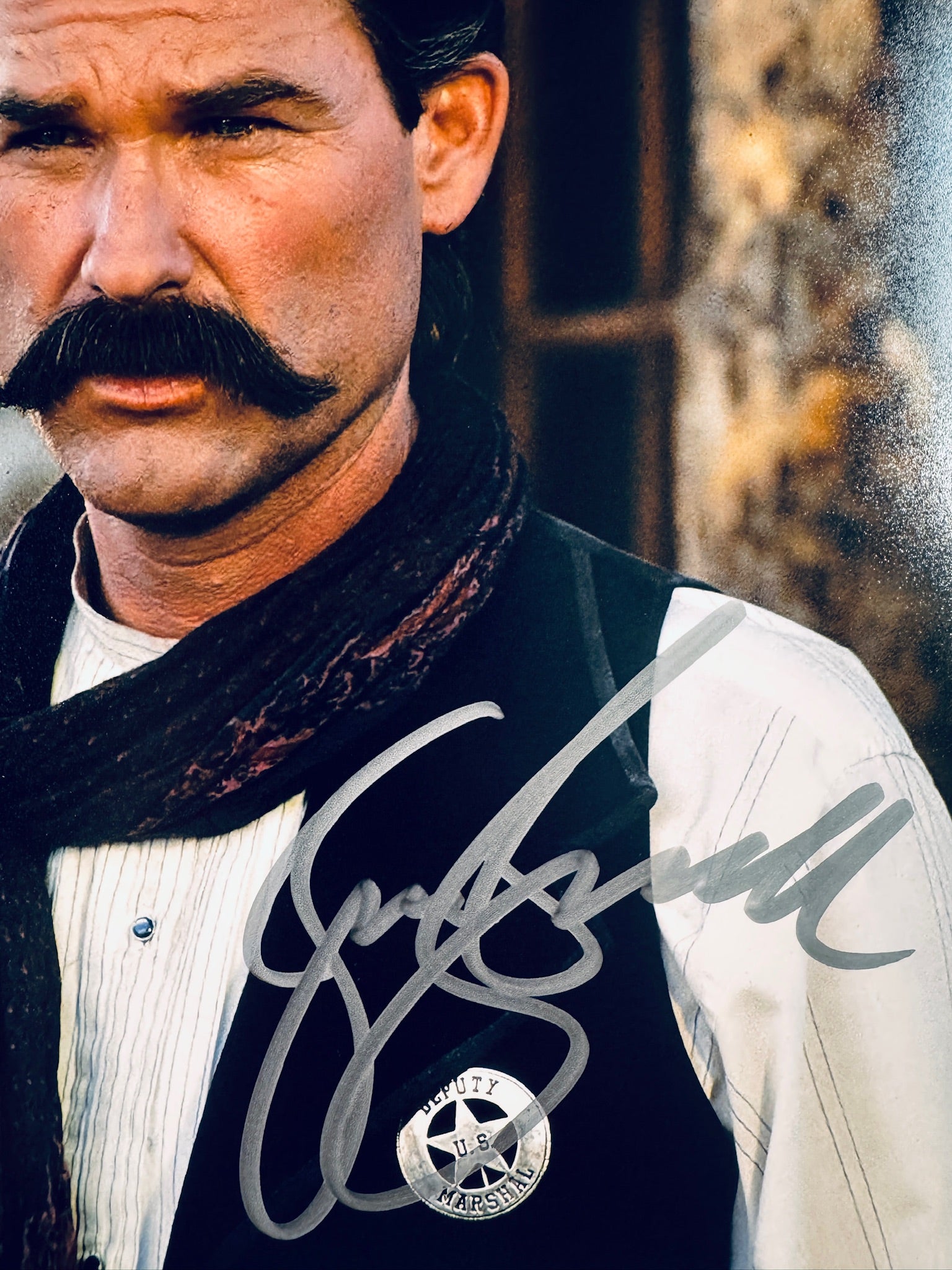 Close-up view of Kurt Russell's signature in silver marker on his Tombstone promotional photo next to the Deputy Marshal badge.