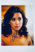 Signed full photo of Lacey Chabert wearing an orange-yellow shirt with pearl earrings, featuring a blue autograph.